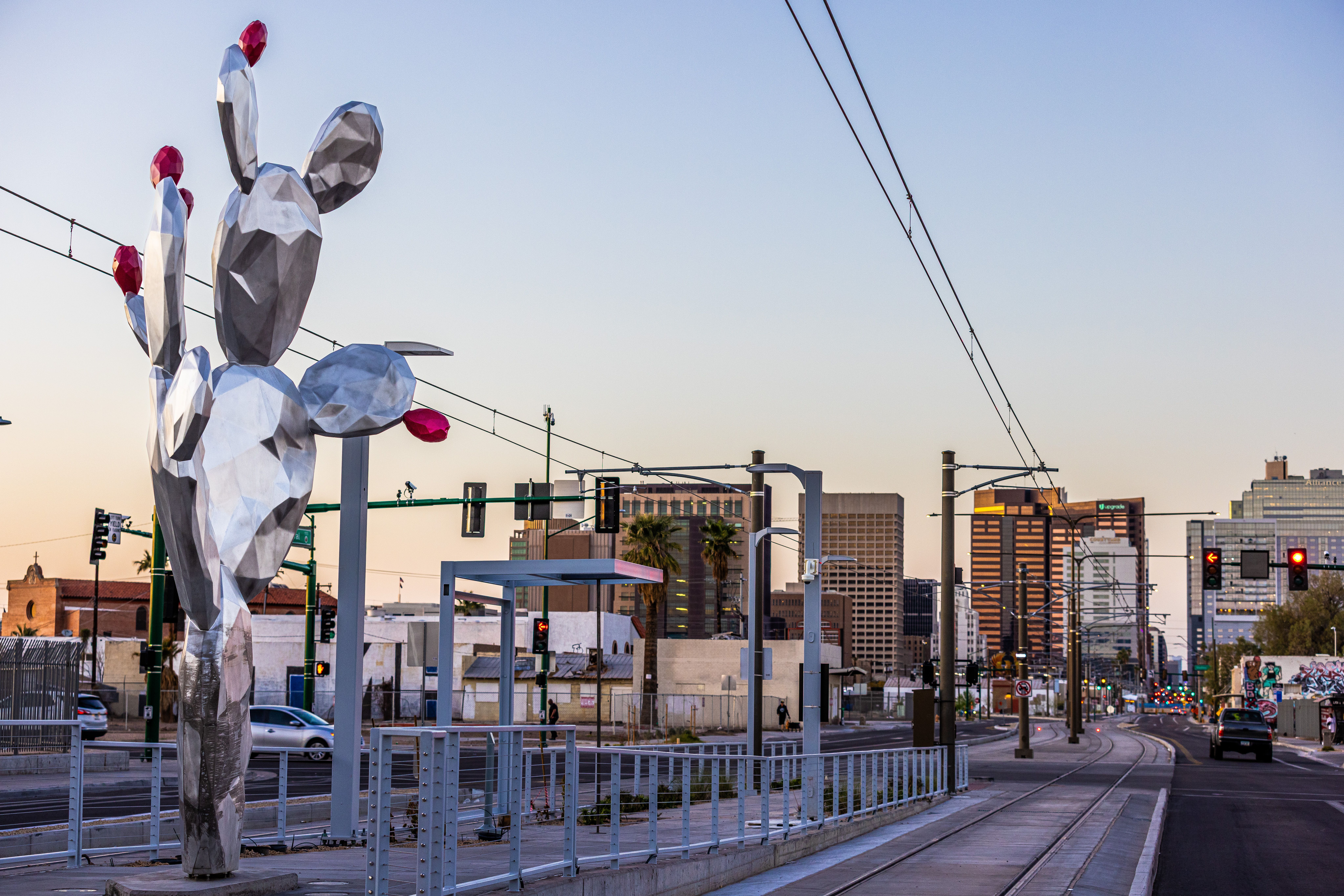 A large prickly pear cactus sculpture made from shiny, silver metal, adorned with bright red fruits. 
