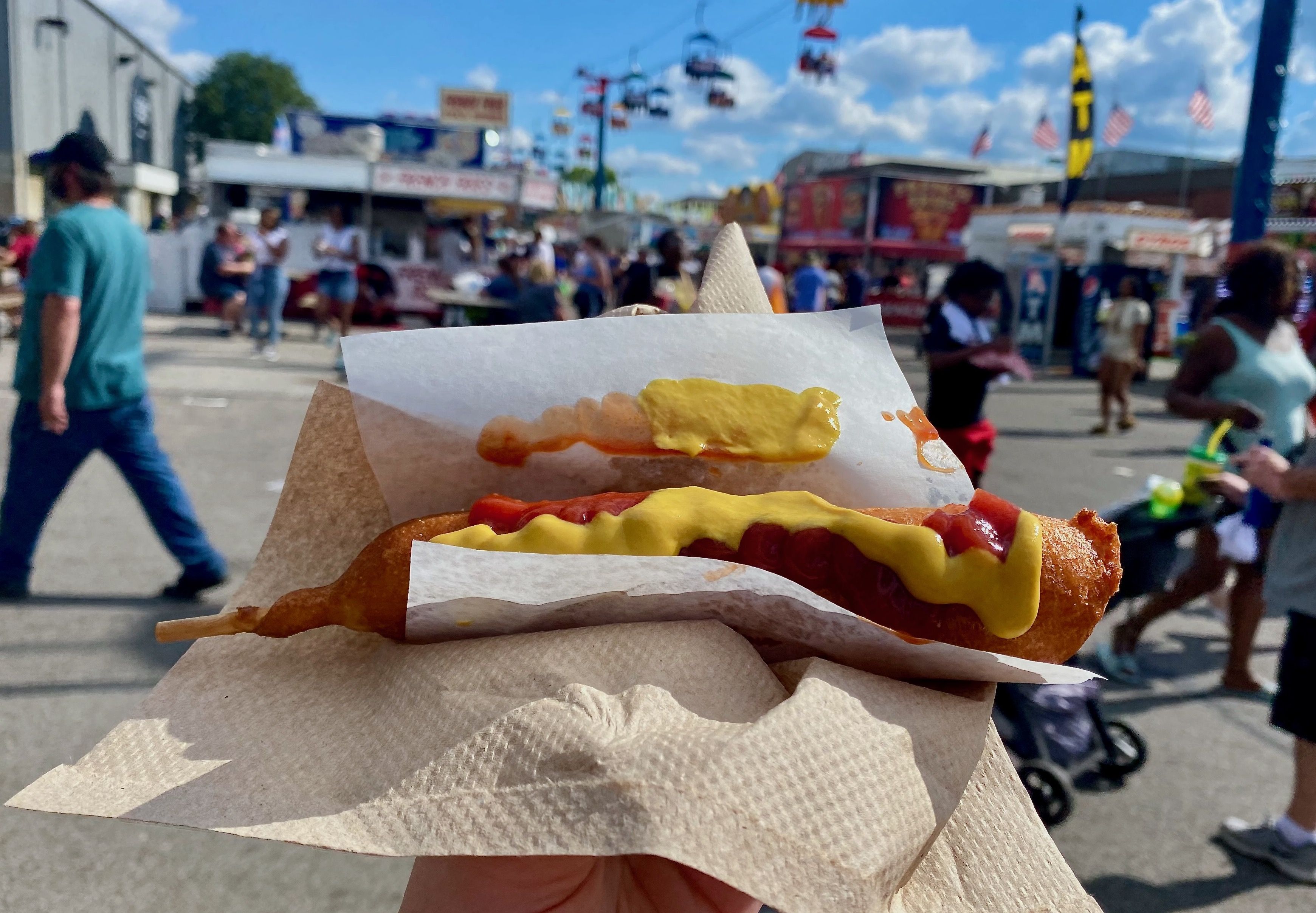 A corn dog covered in ketchup in mustard in the foreground with the SkyGlider ride in the background
