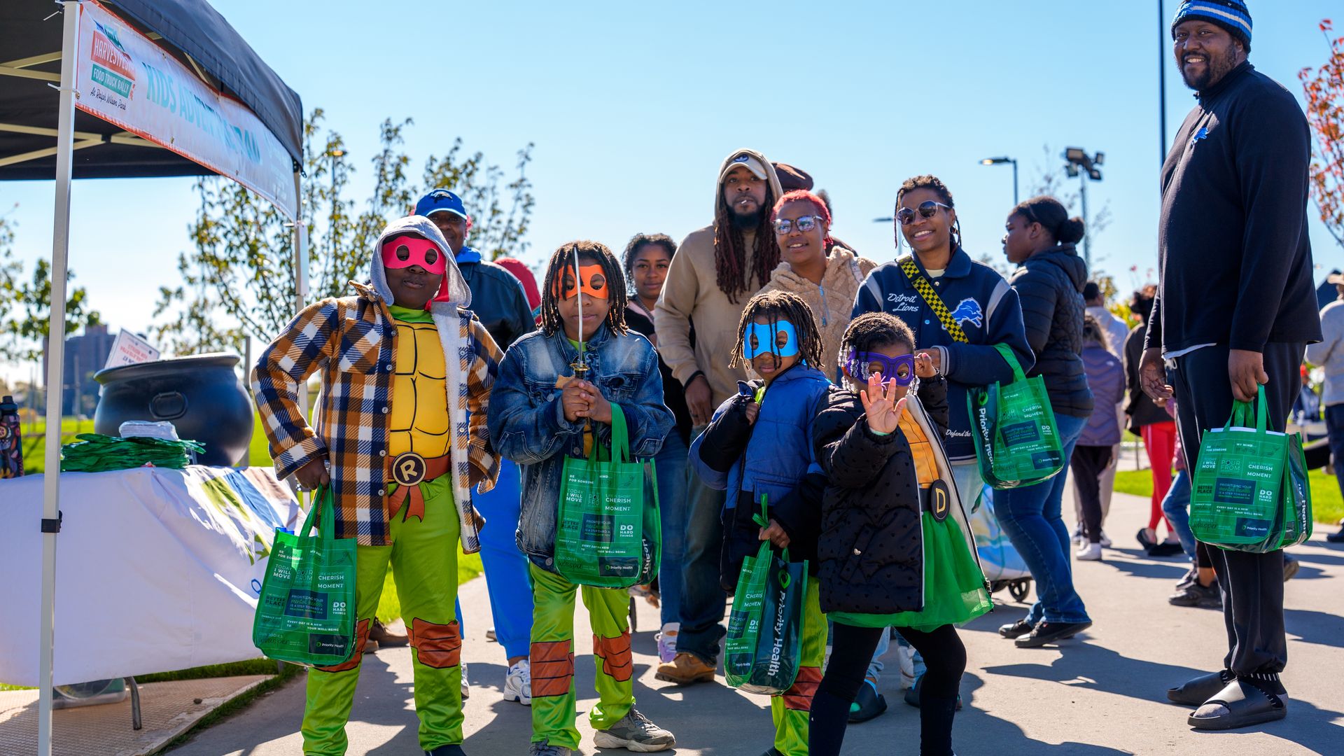 Group of kids and adults outside at the park. The kids are dressed as the teenage mutant ninja turtles.