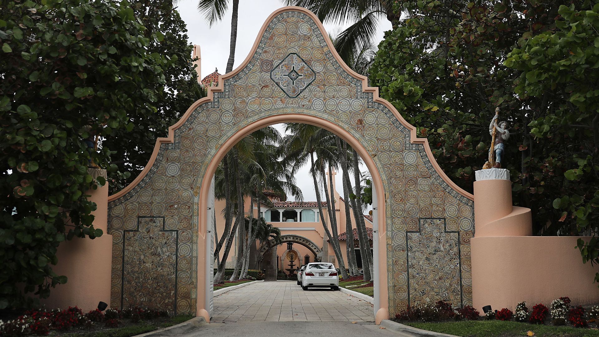 This image shows a stone entranceway to Mar-a-lago, framed by palm trees.