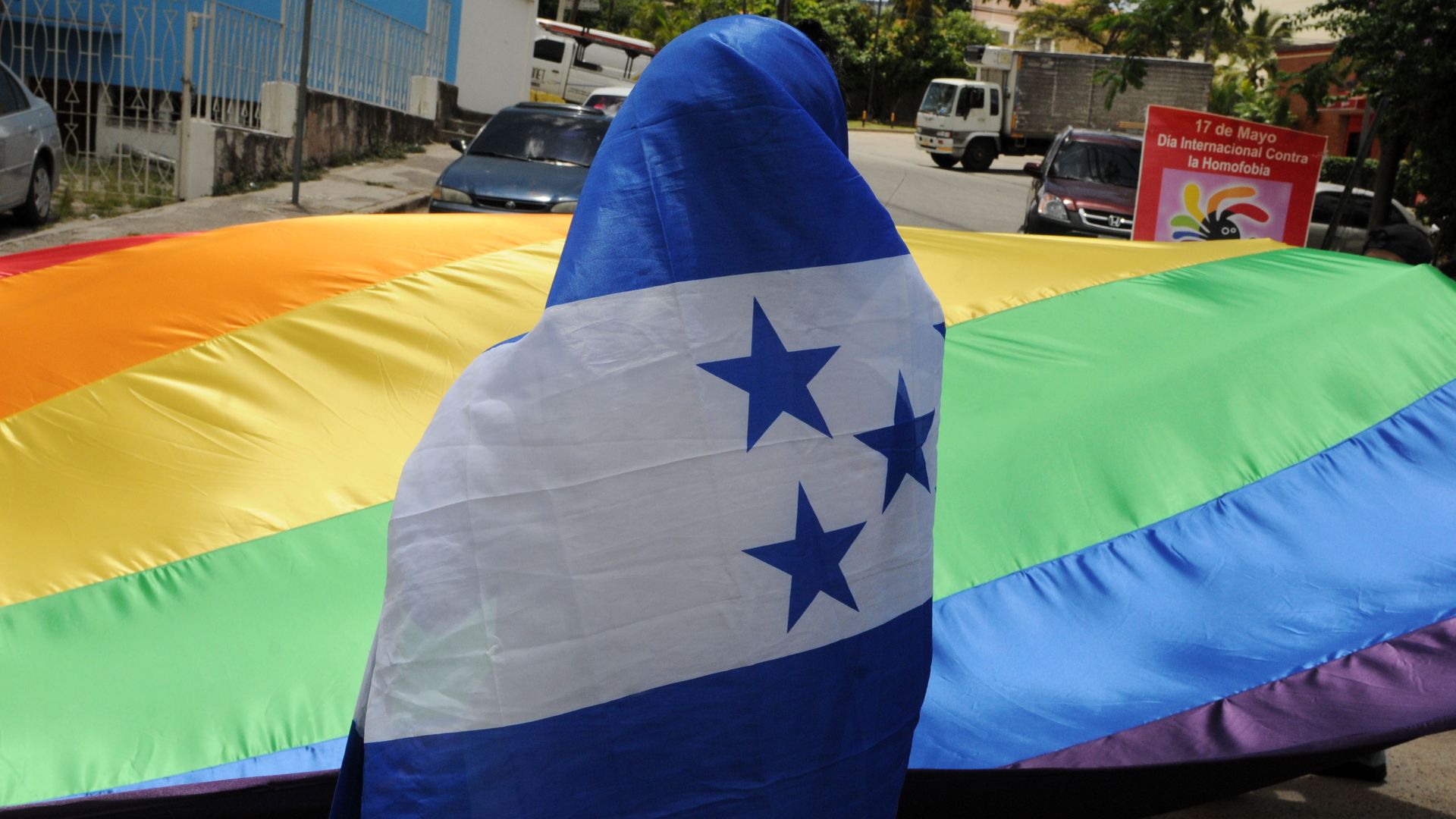 Photo of a person wrapped in the Honduran flag looking at an LGBTQ rainbow flag held in the air