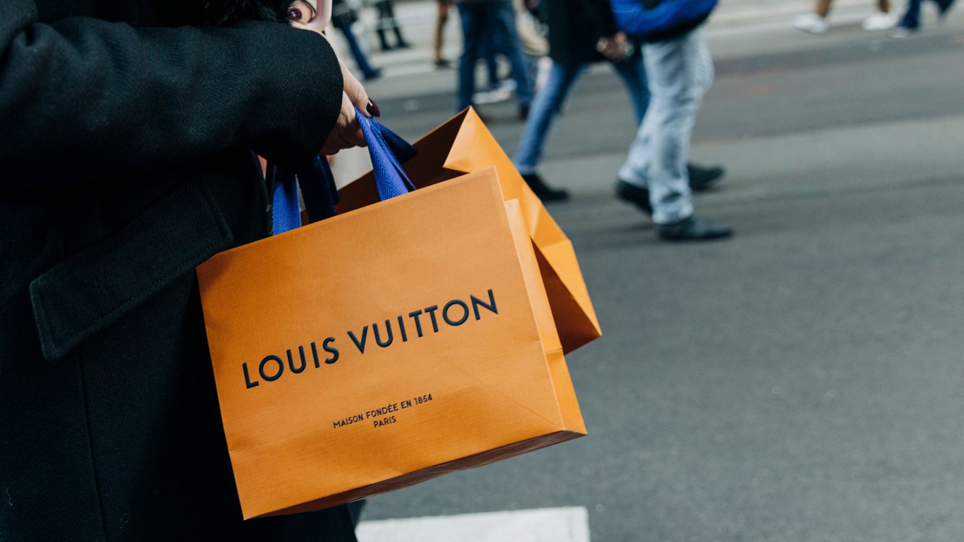 Person carrying a Louis Vuitton shopping bag and walking down a busy street. 