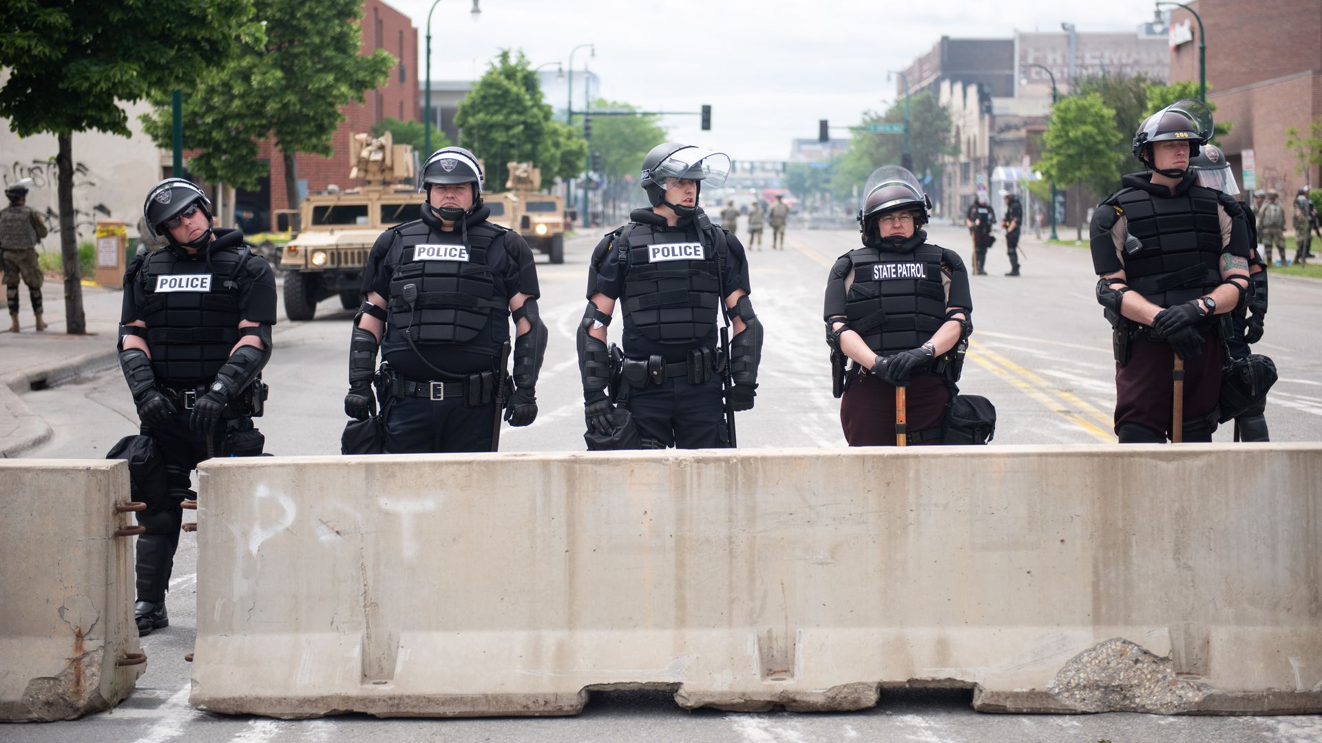 A line of cops stand next to a concrete barrier