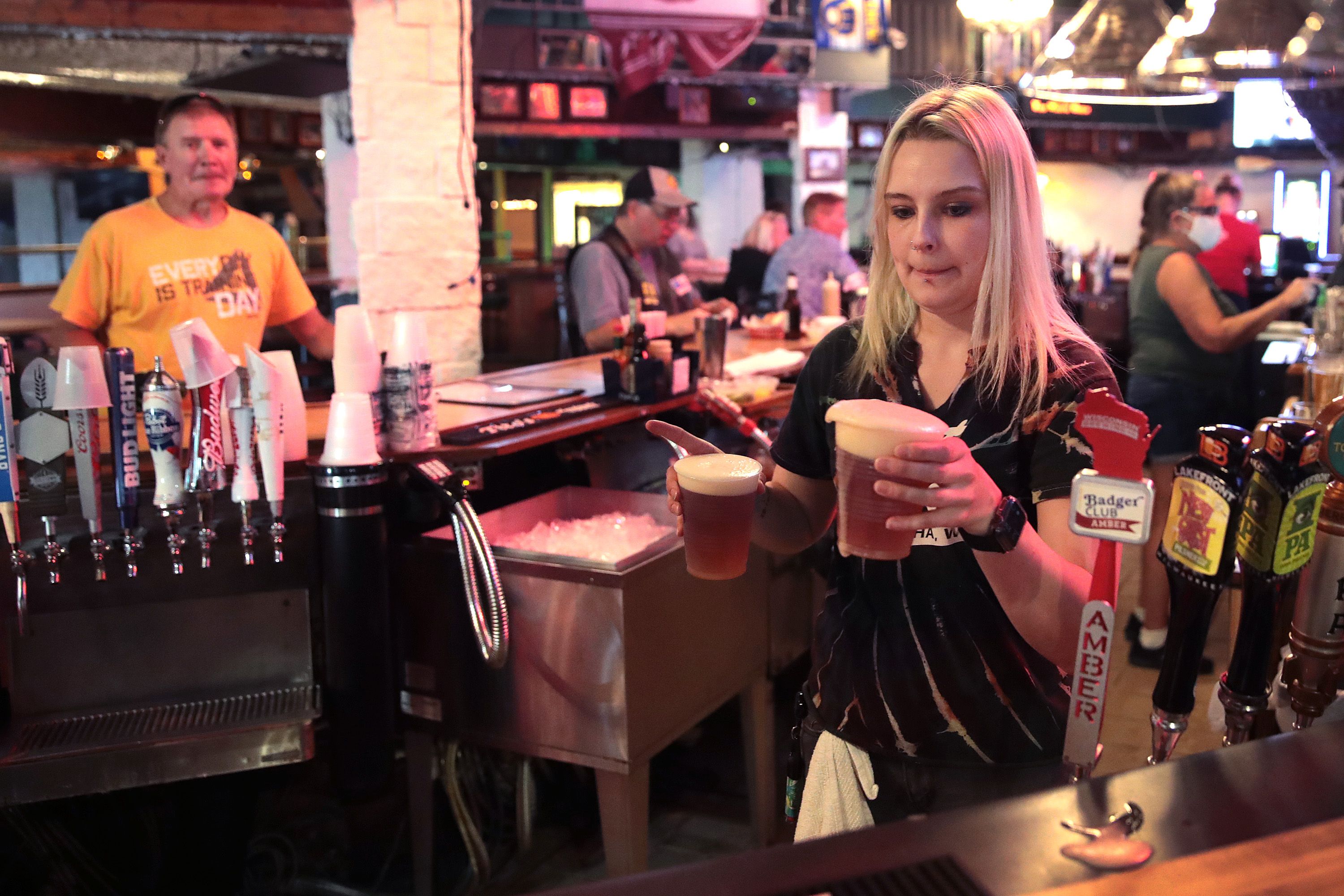 In this image, a female server carries two plastic cups of beer behind the bar counter