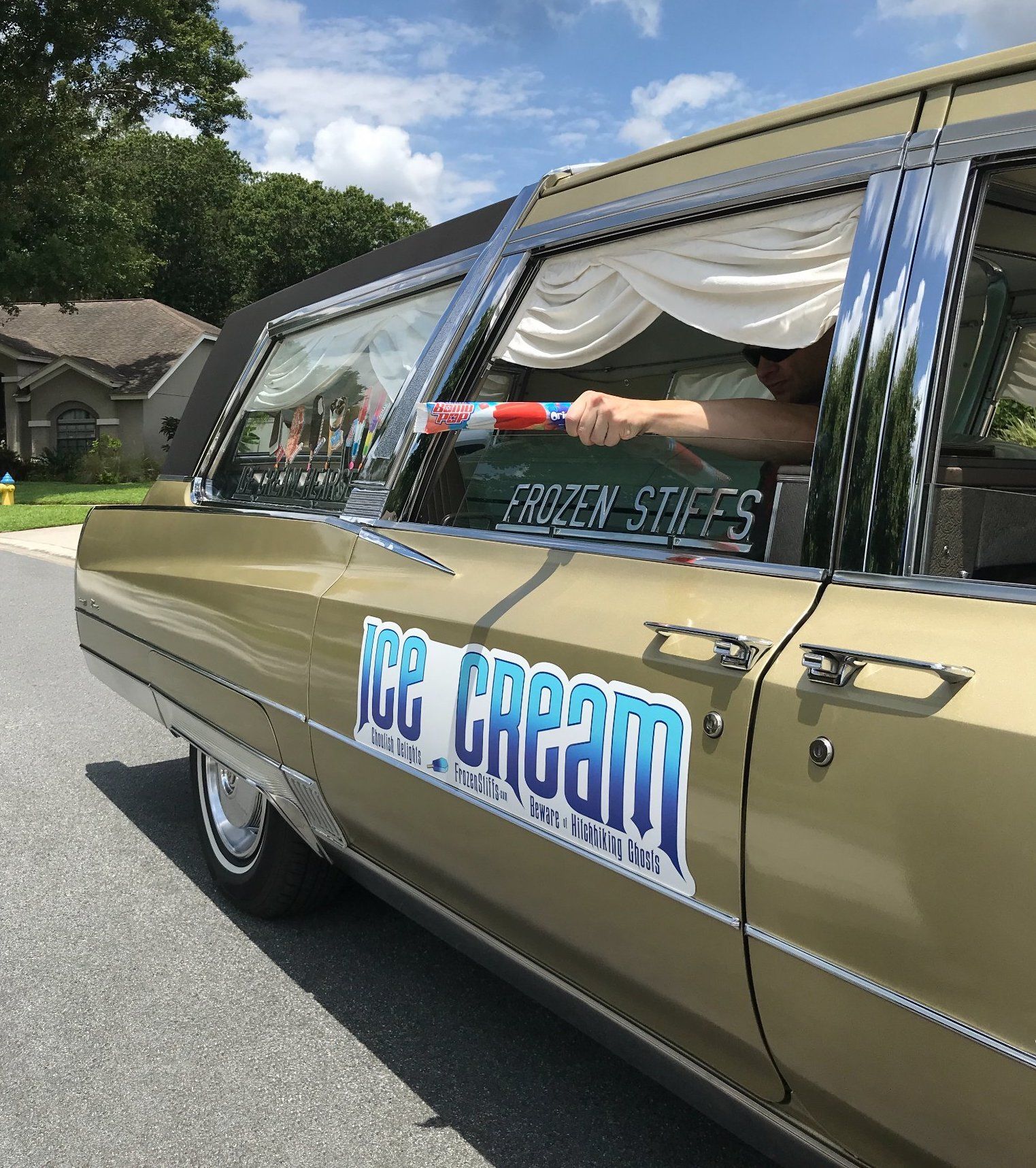 A man's hand holds a popsicle out the window of an ice cream hearse.