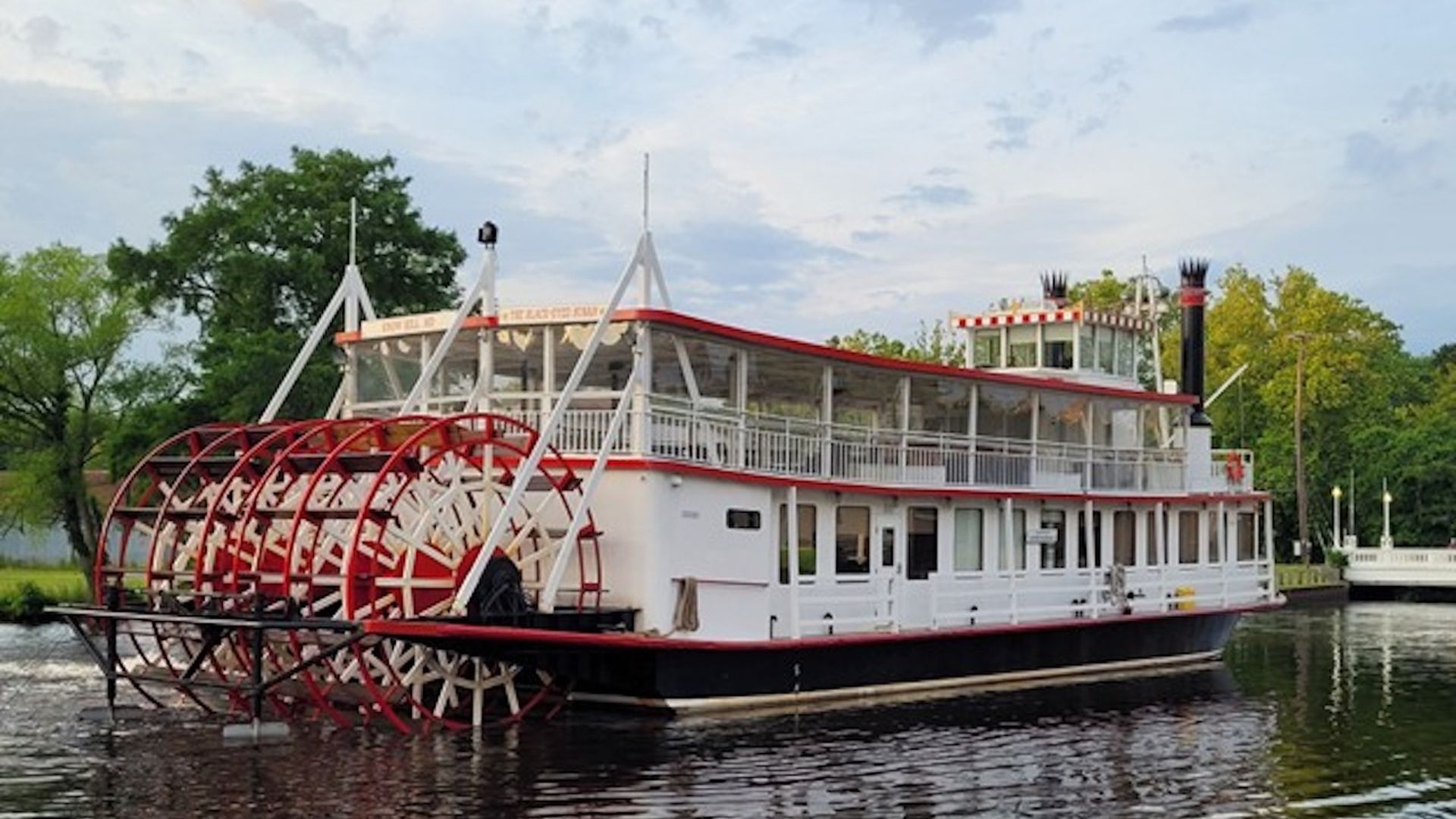 A white and red Victorian-style paddleboat on a river.
