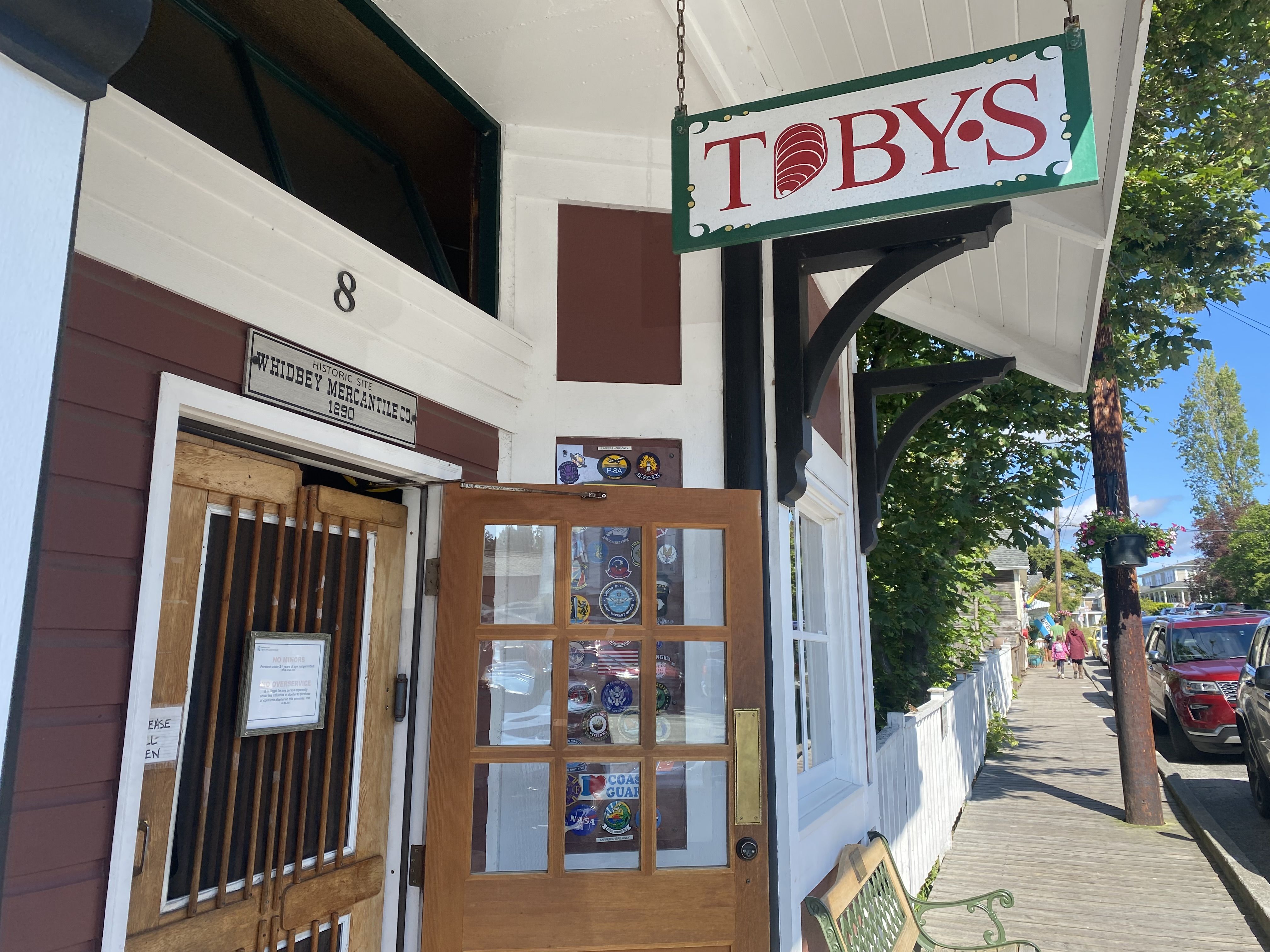 A view of an open door to a painted building with a hanging sign that reads "Toby's" in red letters, with the 'O'  in the shape of a shell.