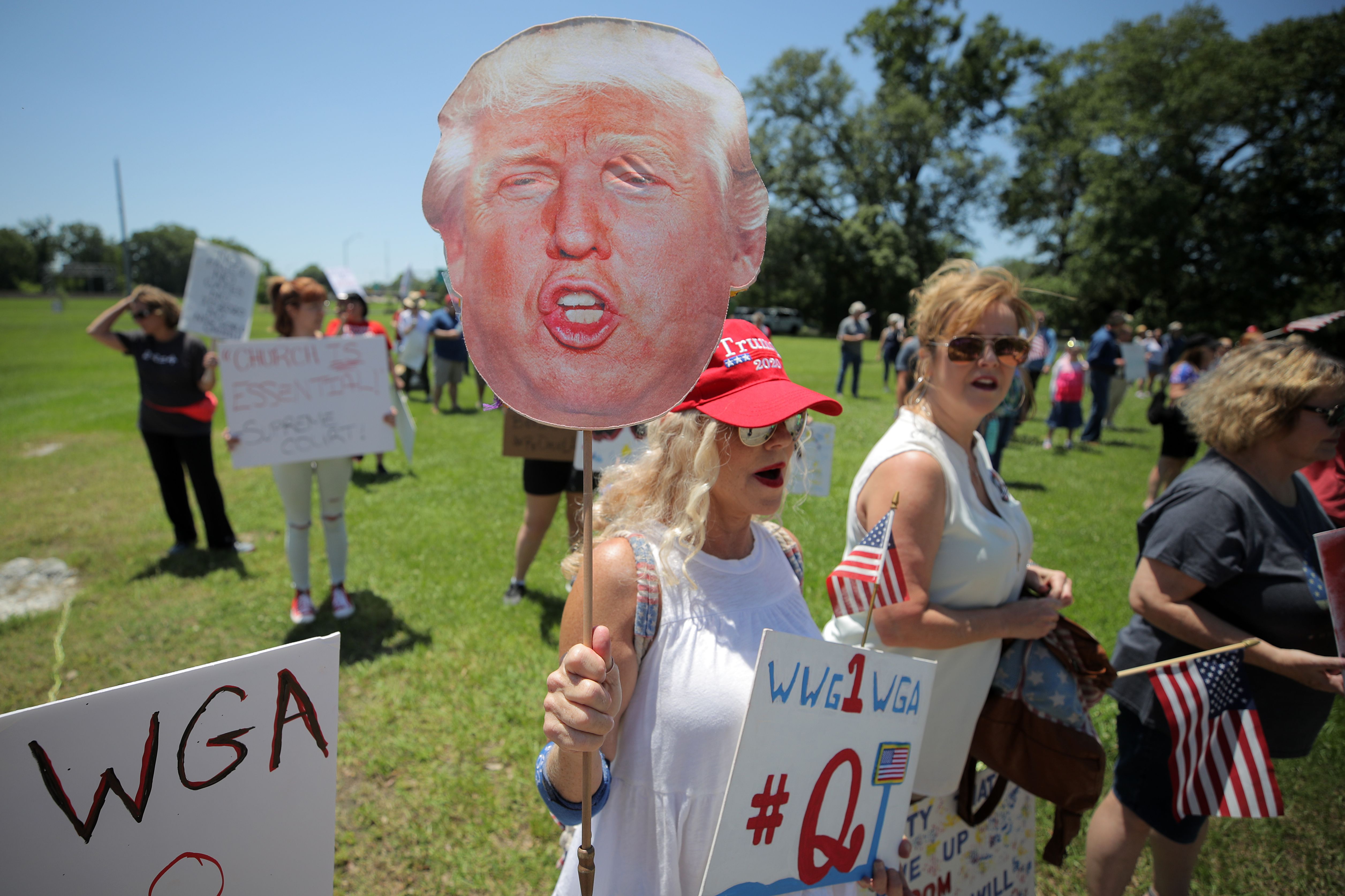 In this image, a woman holds a sign of Trump's face
