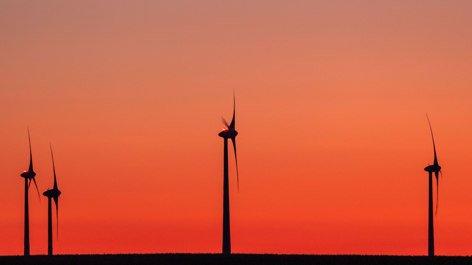 The sun sets behind a series of wind turbines.