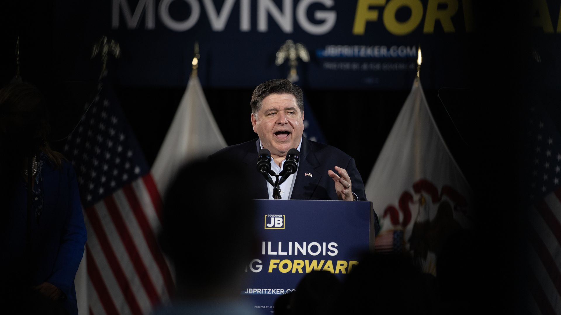 Photo of a man behind a podium making a speech in front of a crowd. 