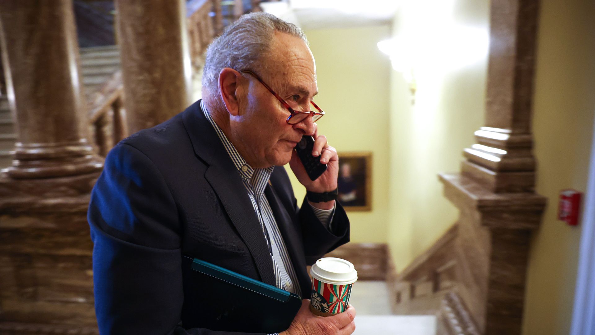 A person holding a coffee cup is talking on their cell phone while walking
