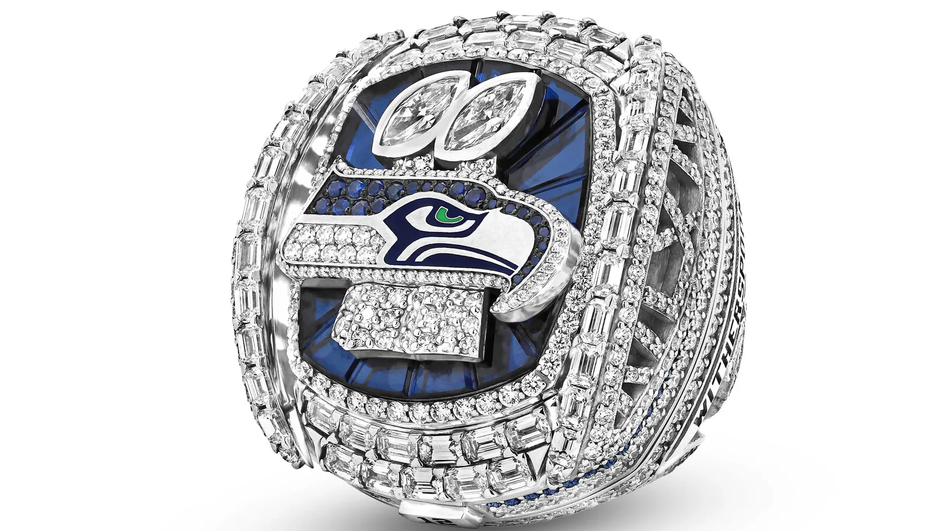 Close-up of a diamond-encrusted ring featuring the Seattle Seahawks logo with a blue enamel background, white and blue hawk-eye design, surrounded by multiple rows of sparkling diamonds.