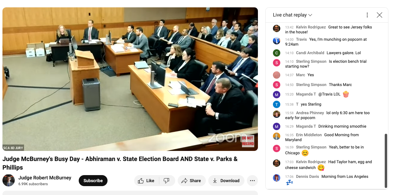 A screenshot of a YouTube channel livestreaming attorneys sitting at tables and a packed courtroom gallery