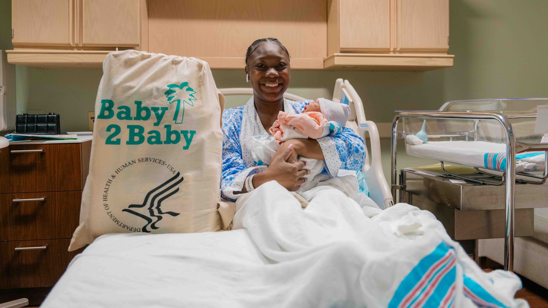 Photo shows a new mom in a hospital bed with her child and a Baby 2 Baby care kit