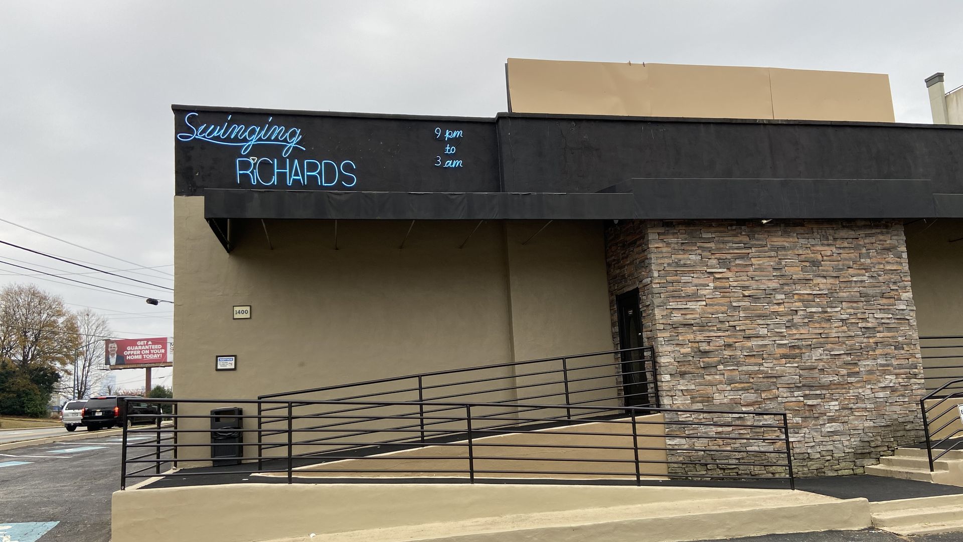 A squat brown building with a dark roof overhang with a neon sign that says "Swinging Richards"