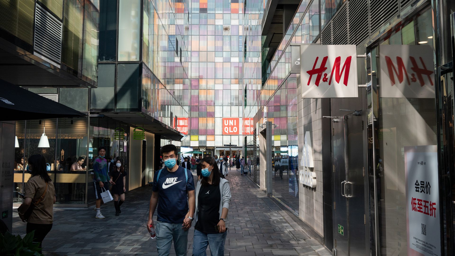 People wearing protective masks walk past a Hennes & Mauritz AB (H&M) store and a Uniqlo store, operated by Fast Retailing Co., at a shopping area in Beijing, China on Sunday, Sept. 20