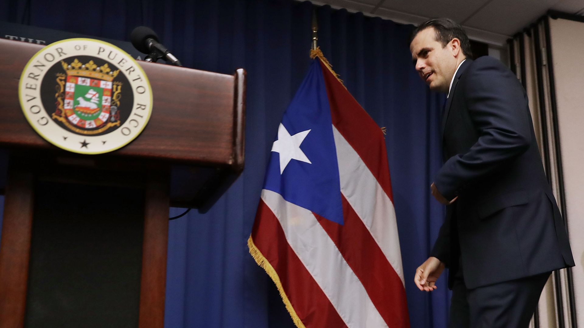 Puerto Rico Gov. Ricardo Rosselló walks up to a podium with the Puerto Rican flag behind him. 