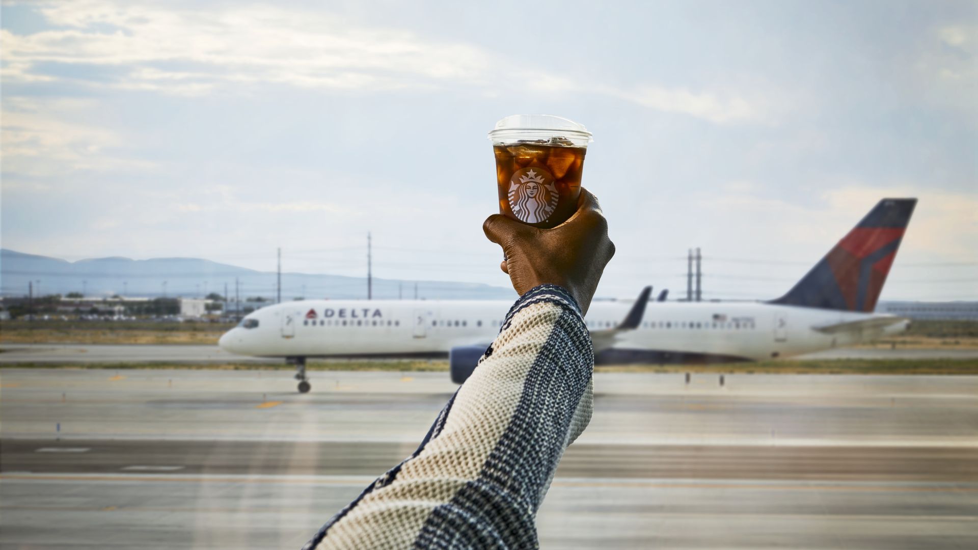 Arm holding a Starbucks cup with a Delta airplane in background