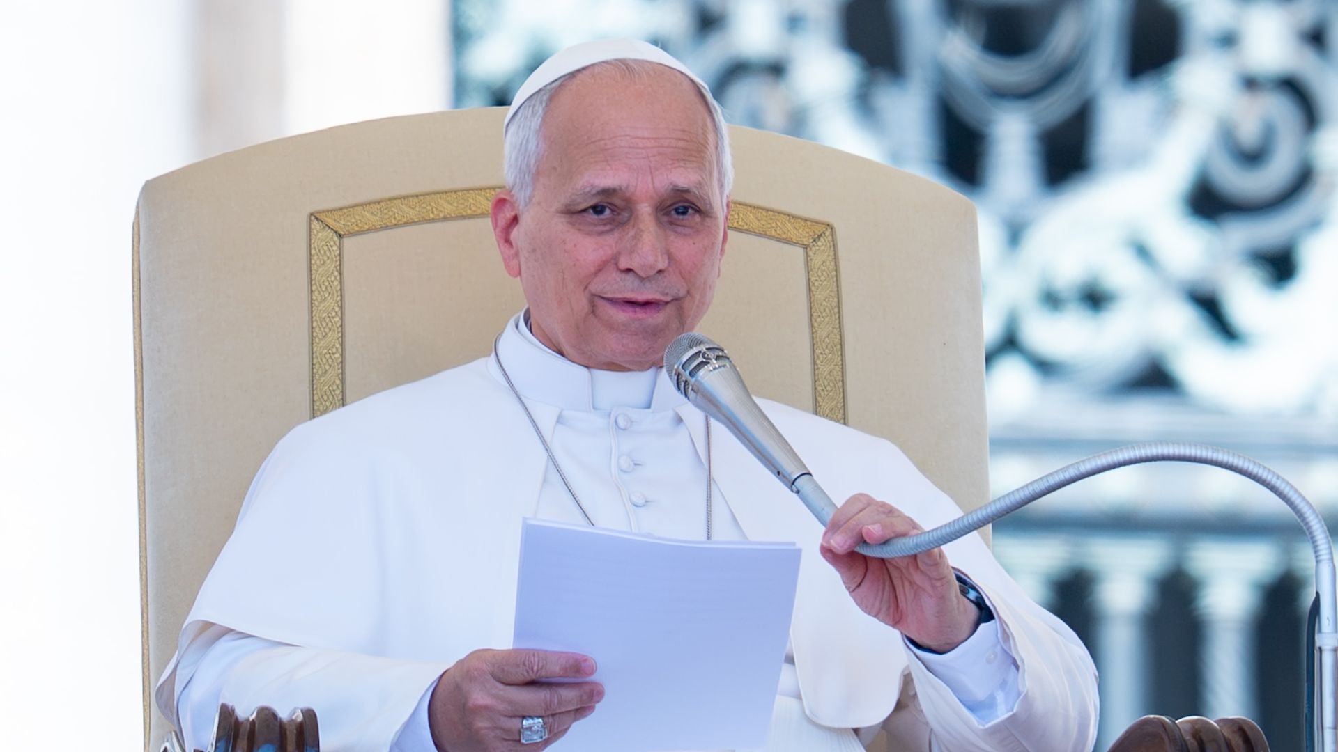 Pope Leo XIV sitting and holding a silver microphone