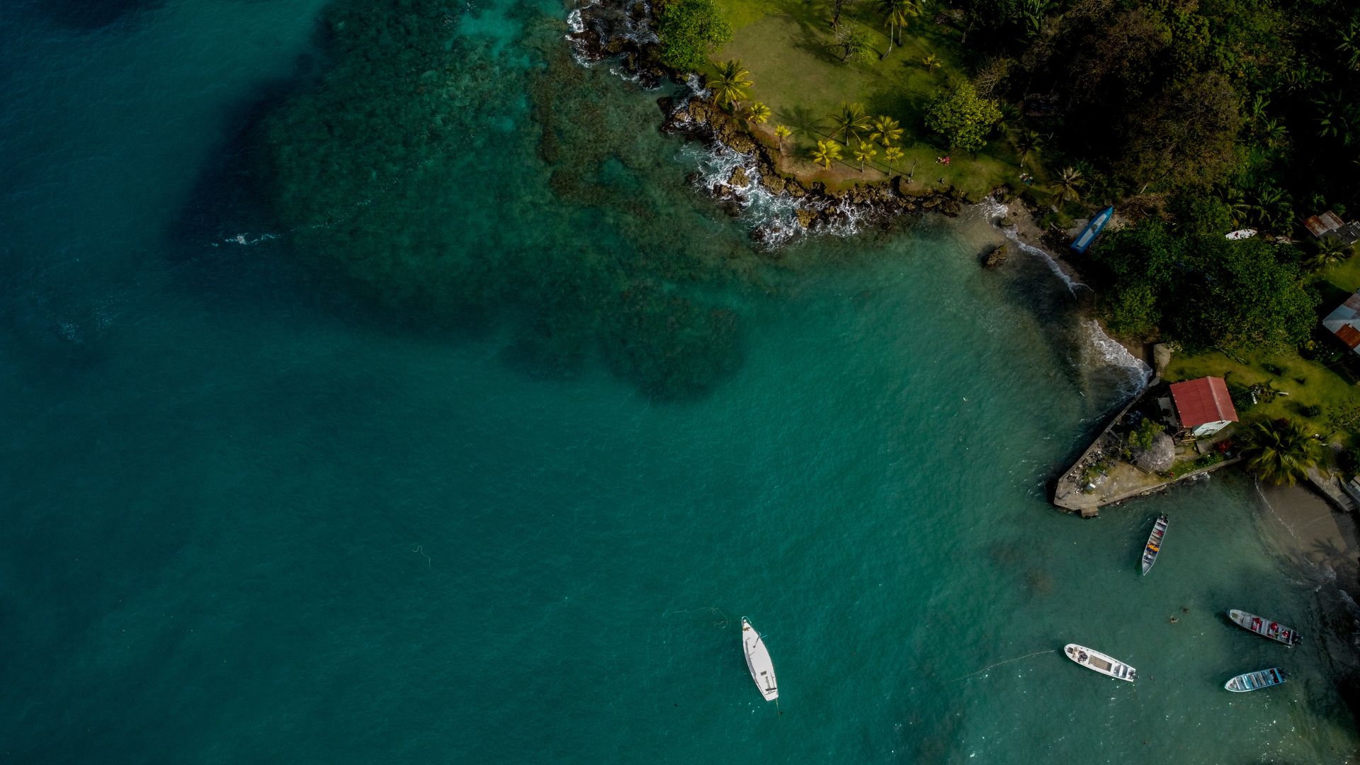 An overhead shot of a Colombian ocean, very green, with a few boats floating on it. Lush green mountains can also be seen. 