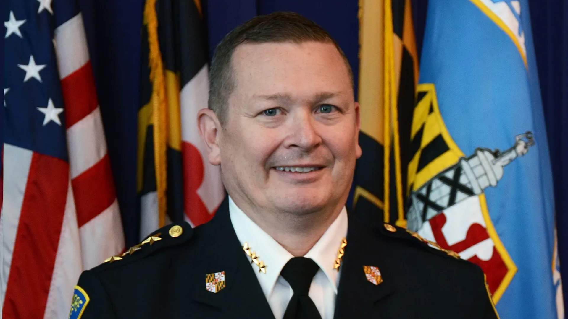 A man posing for a headshot in front of flags.