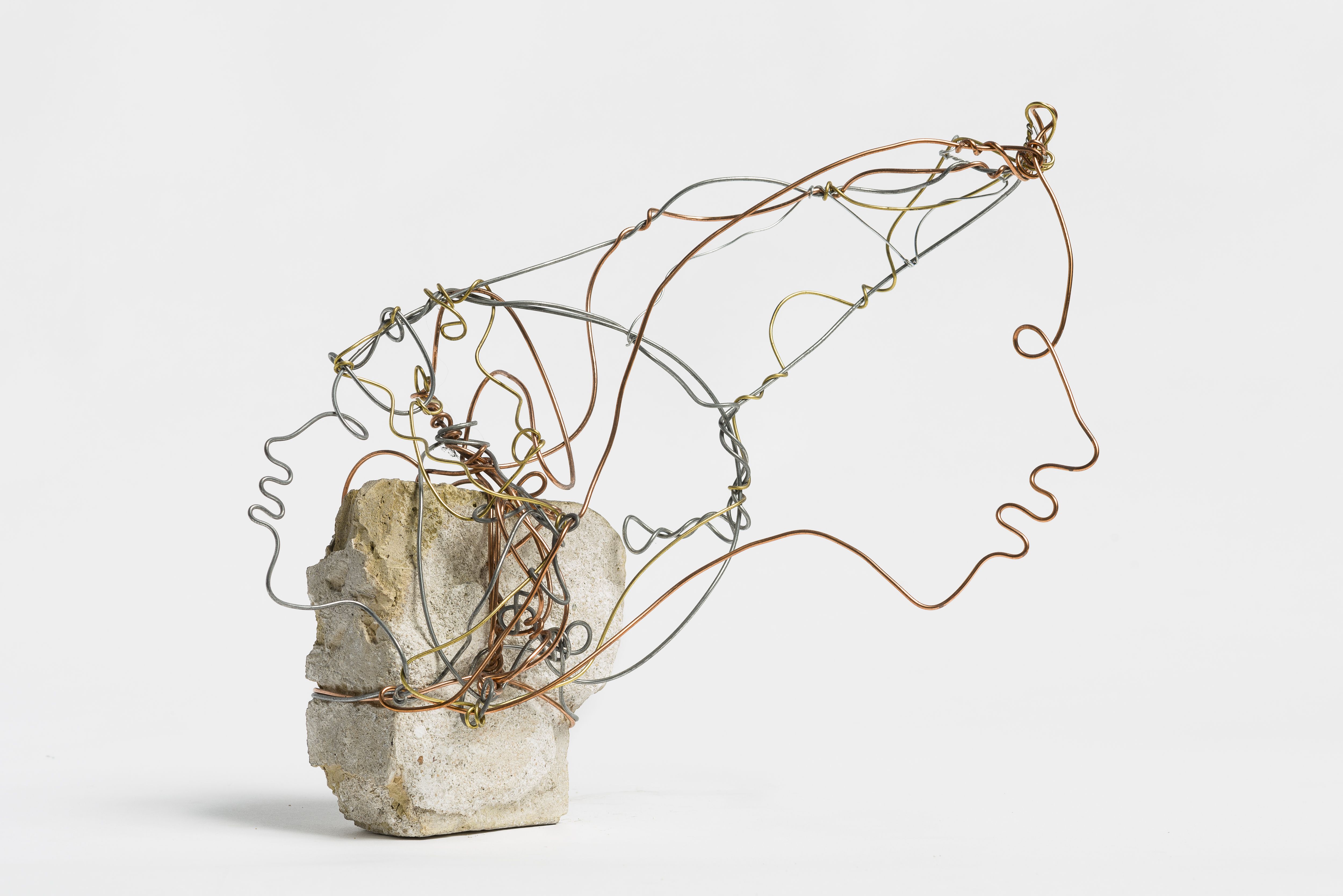 Abstract wire sculpture shaped like two interconnected human profiles, made from silver, copper, and brass wires, mounted on a rough stone base against a white background.