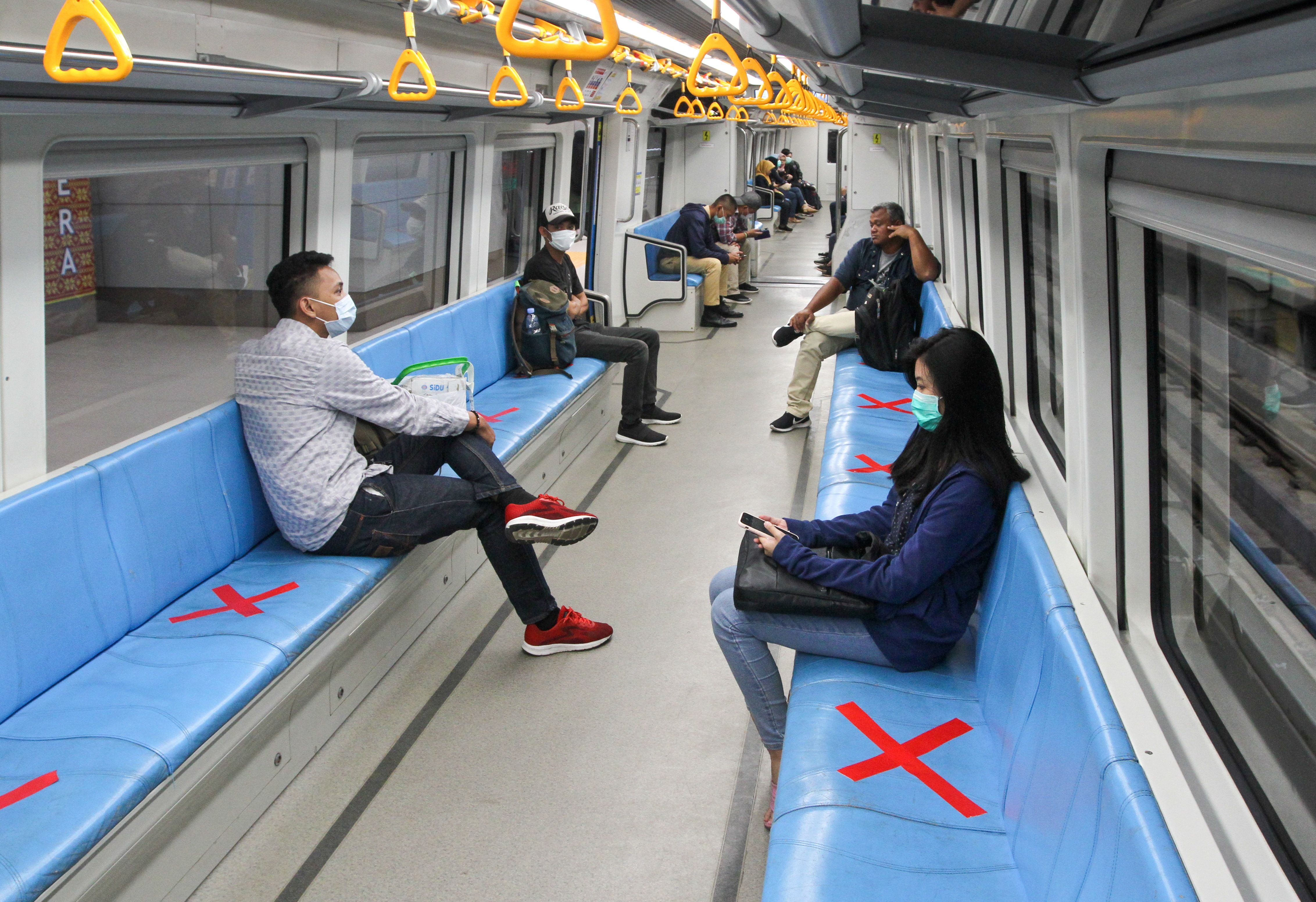 People sit on designated areas decided by red cross marks to ensure social distancing inside a light rapid transit train in Palembang, South Sumatra 