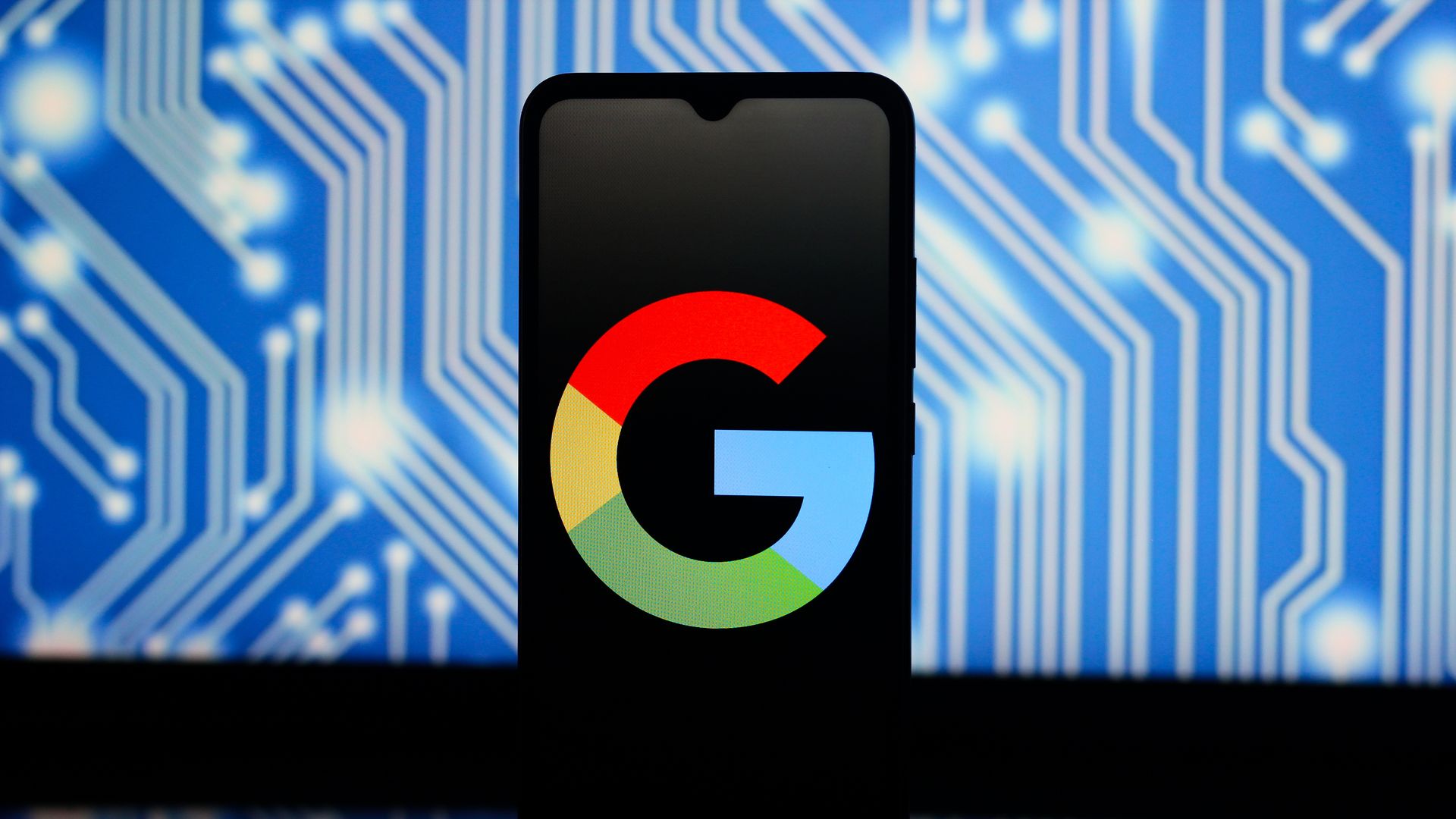 Smartphone showing the colorful Google logo on screen, with a blue circuit board pattern background illuminated and reflected beneath the phone.