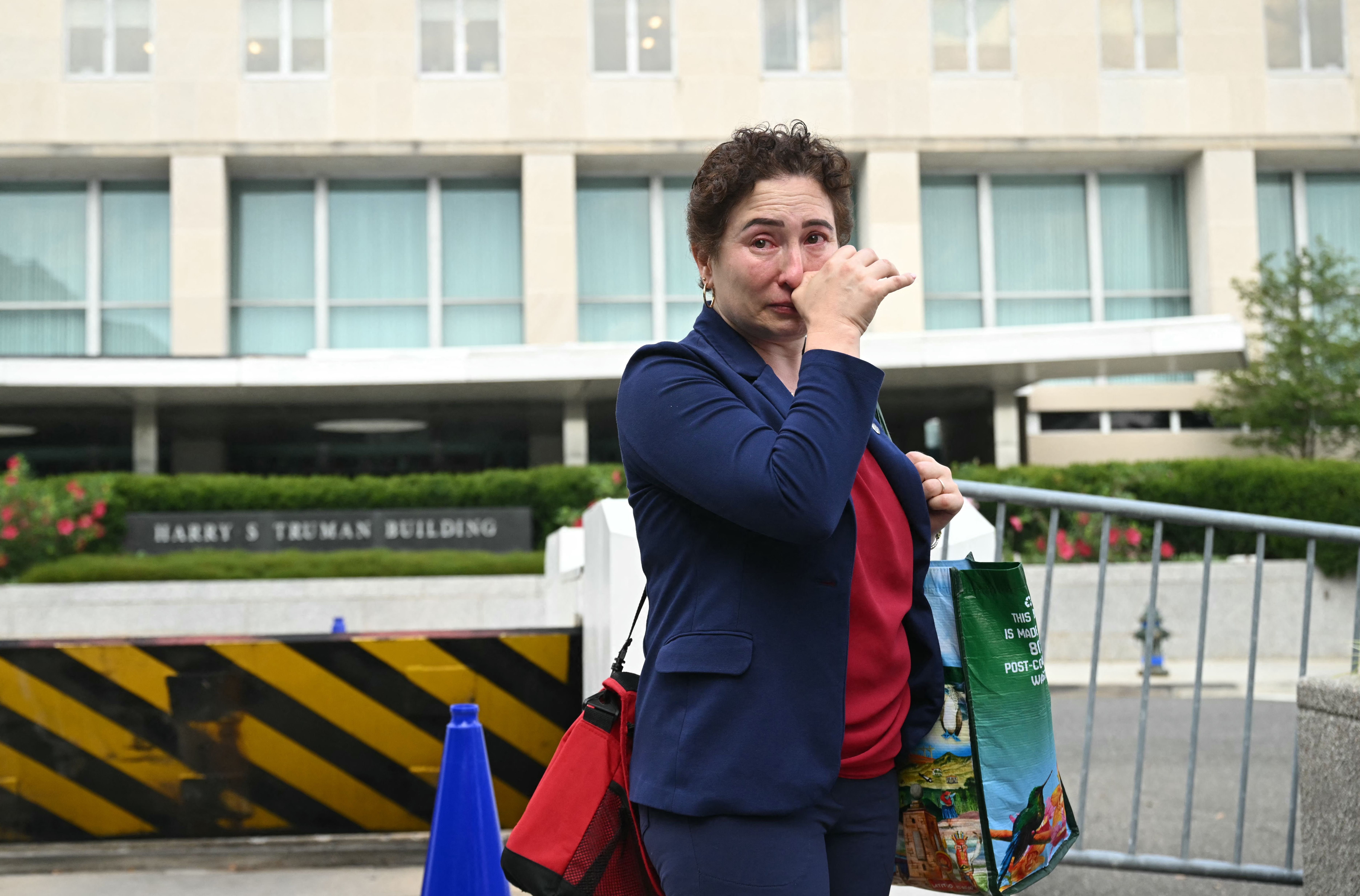 Woman in blue blazer crying, wiping her face as she leaves federal building carrying a lot of personal items. 