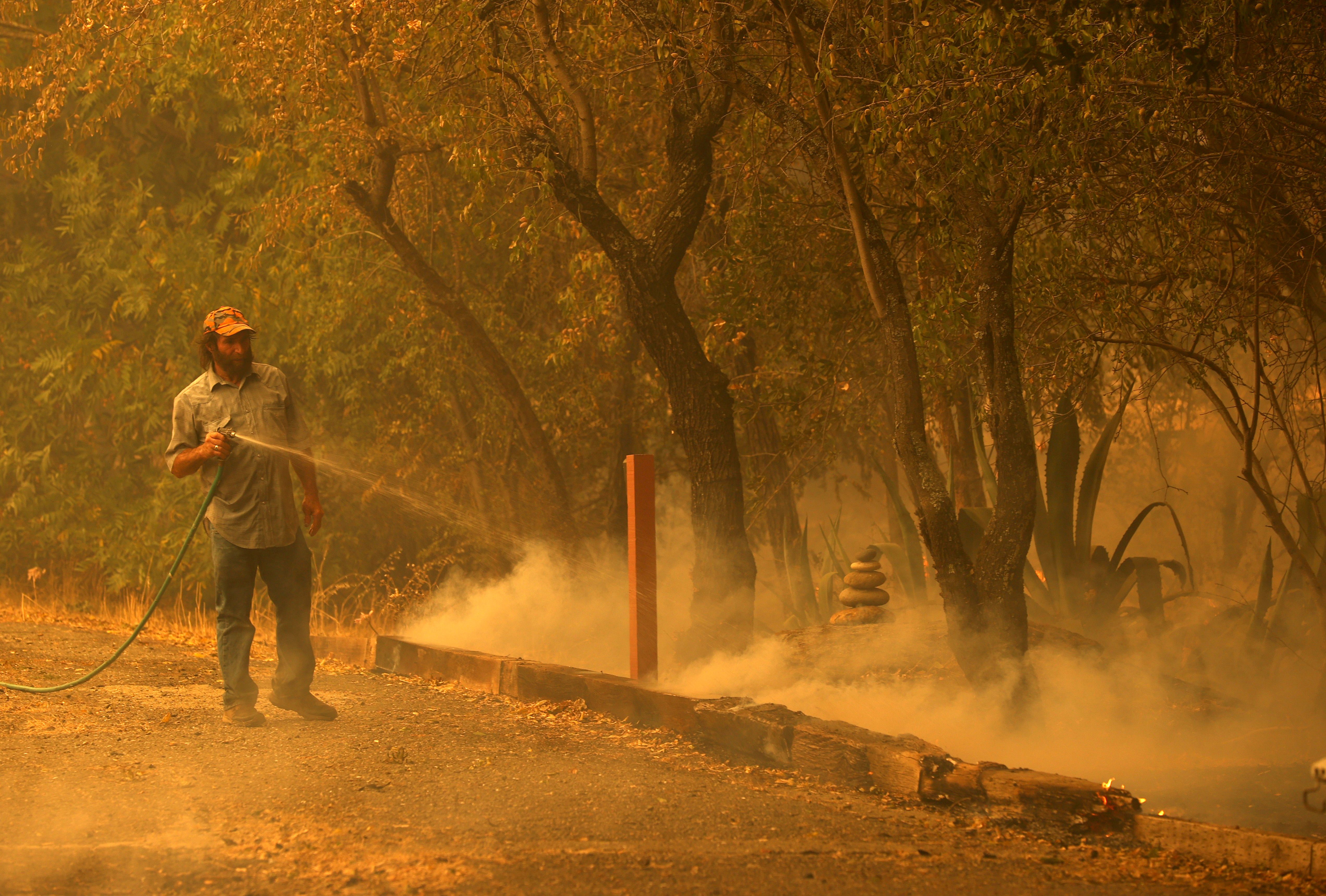 A resident uses a garden hose as he extinguishes spot fires while protecting his property as the LNU Lightning Complex fire burns through the area on August 19