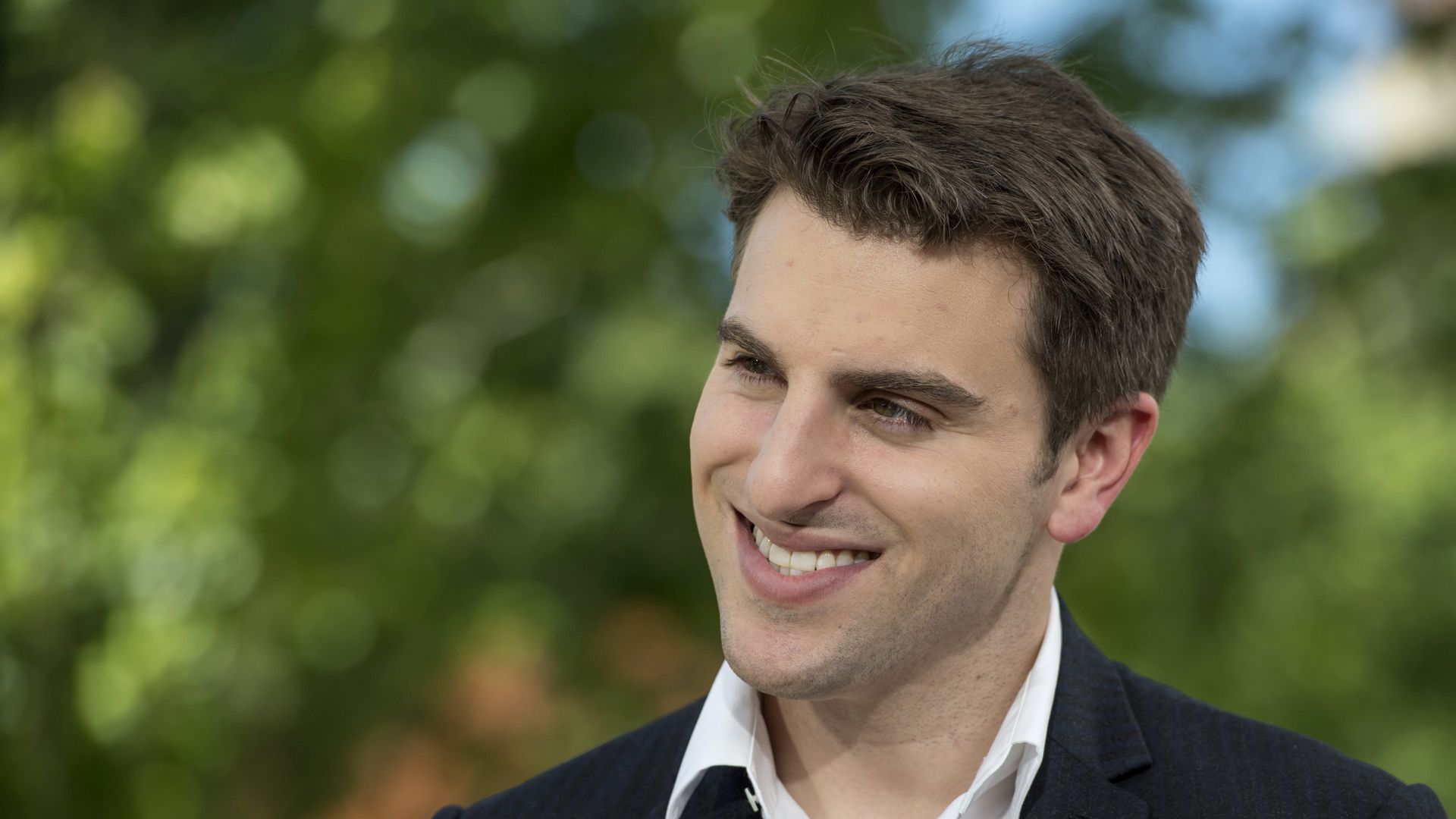 Brian Chesky, man in white button down and black blazer smiling 