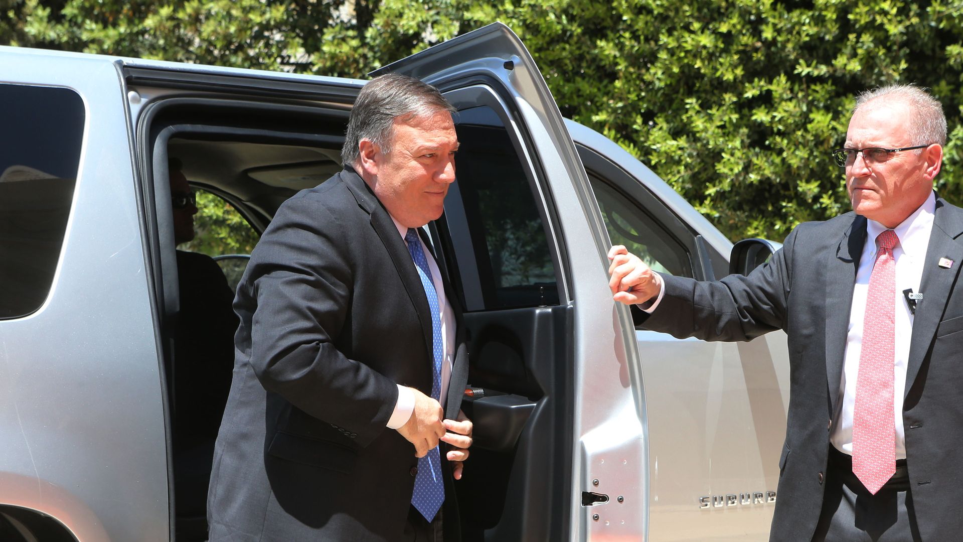 Mike Pompeo pulls his suitcoat together to button it as he steps out of a silver car.