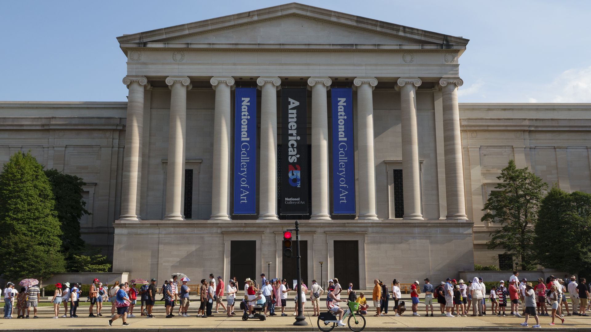 People wait in line near the National Gallery of Art, in front of a banner that says "America's 250."