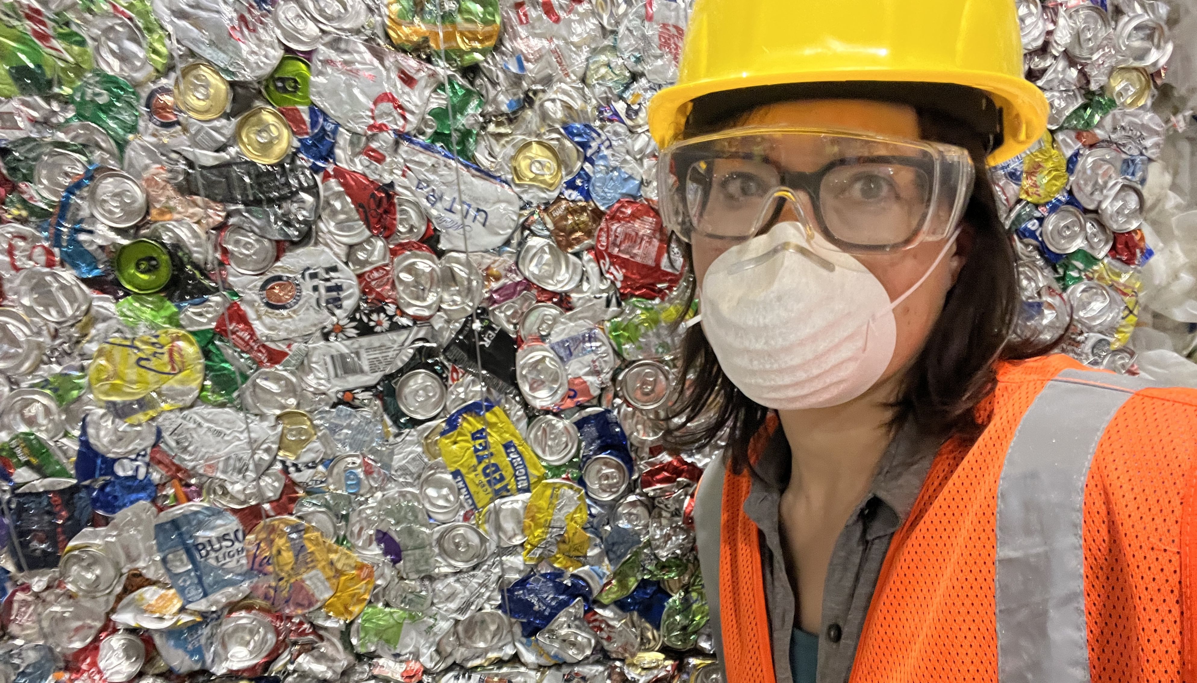 woman in hard hat next to bale of cans 