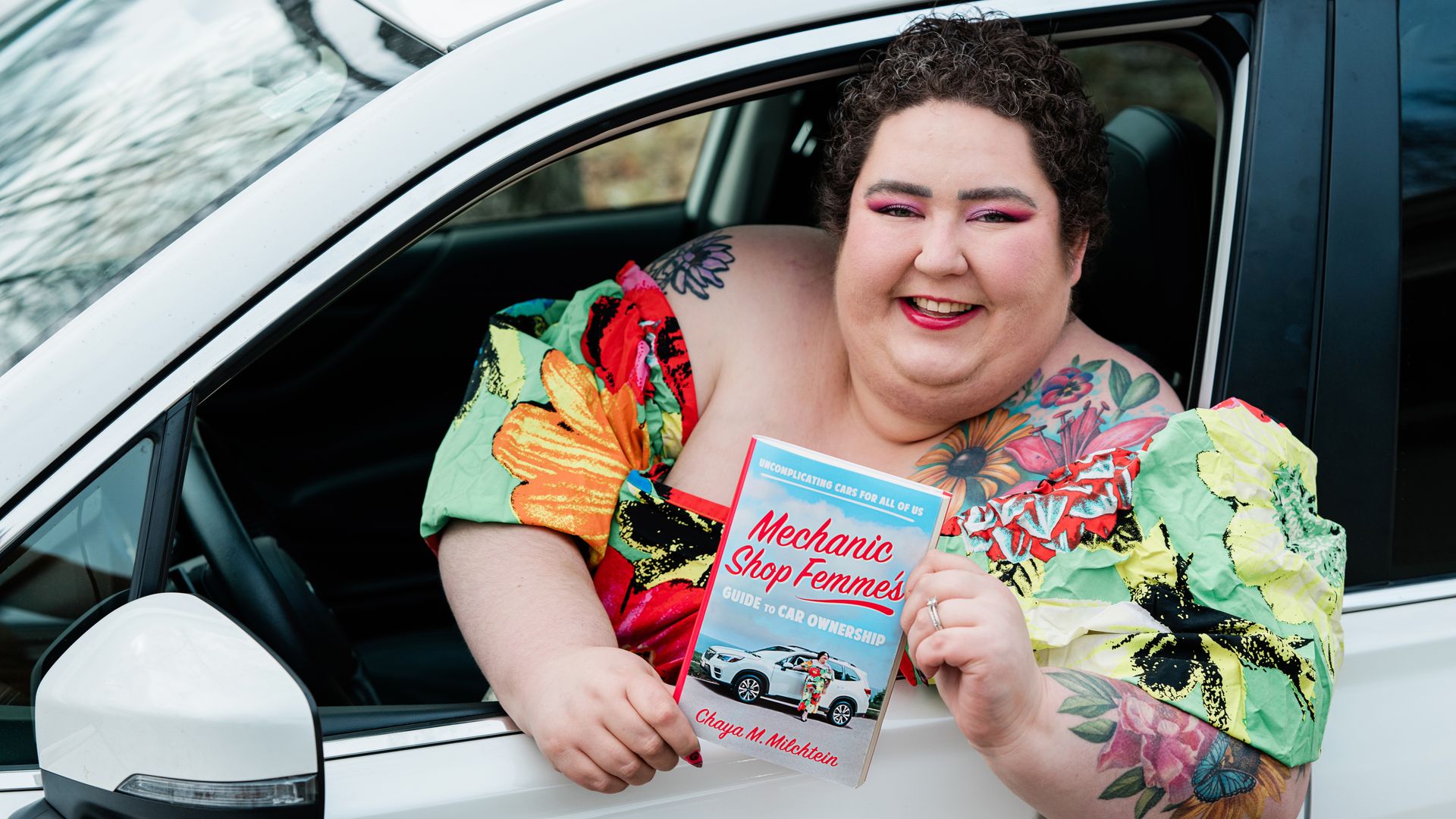 A woman leaning out of her car window holding a book