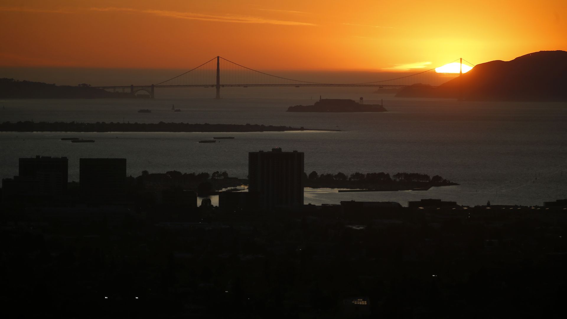 This image shows a dark San Francisco skyline during a sunset, with the darkened Golden Gate bridge in the distance