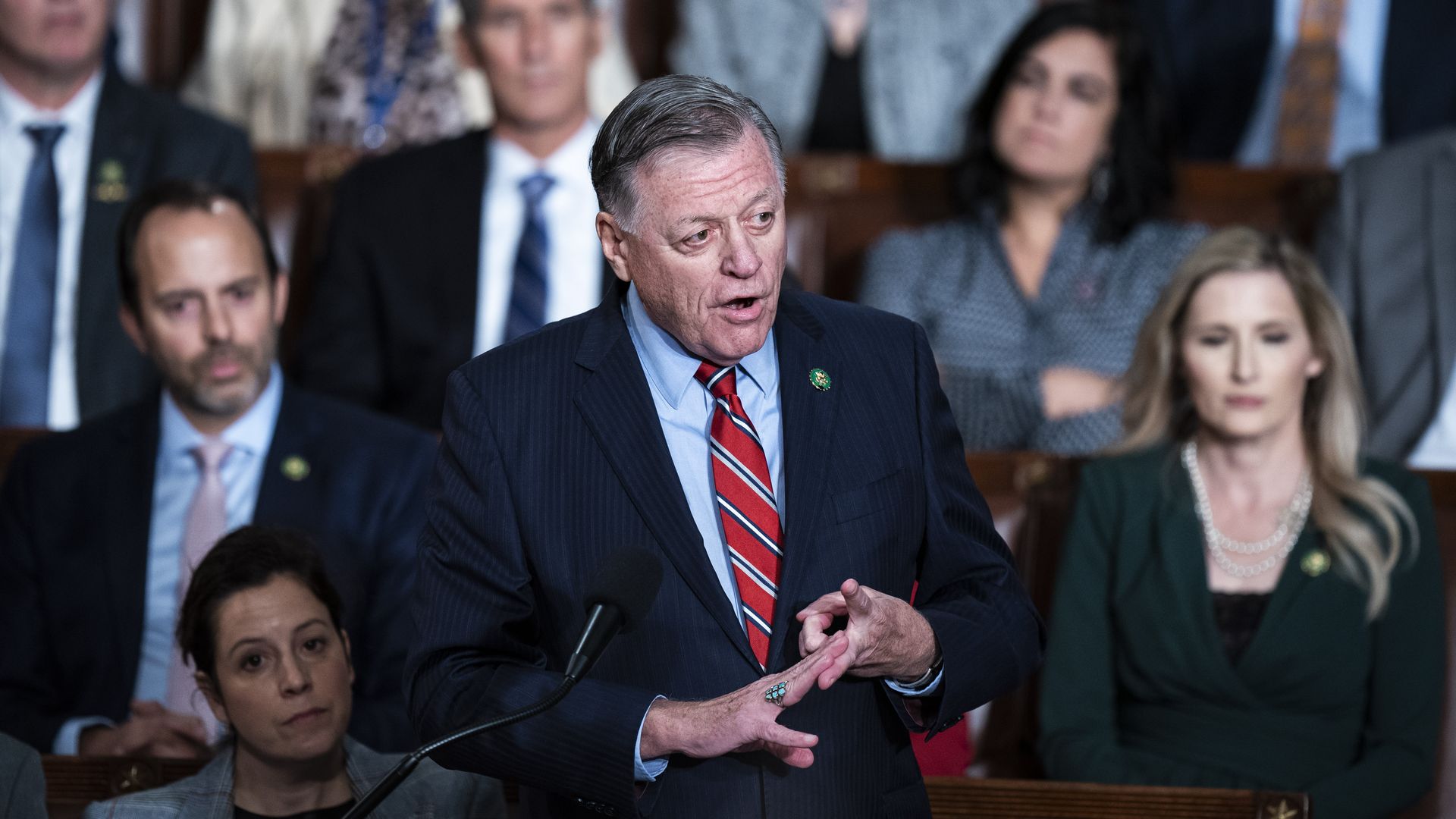 Rep. Tom Cole, wearing a blue suit and speaking on the House floor while surrounded by colleagues.