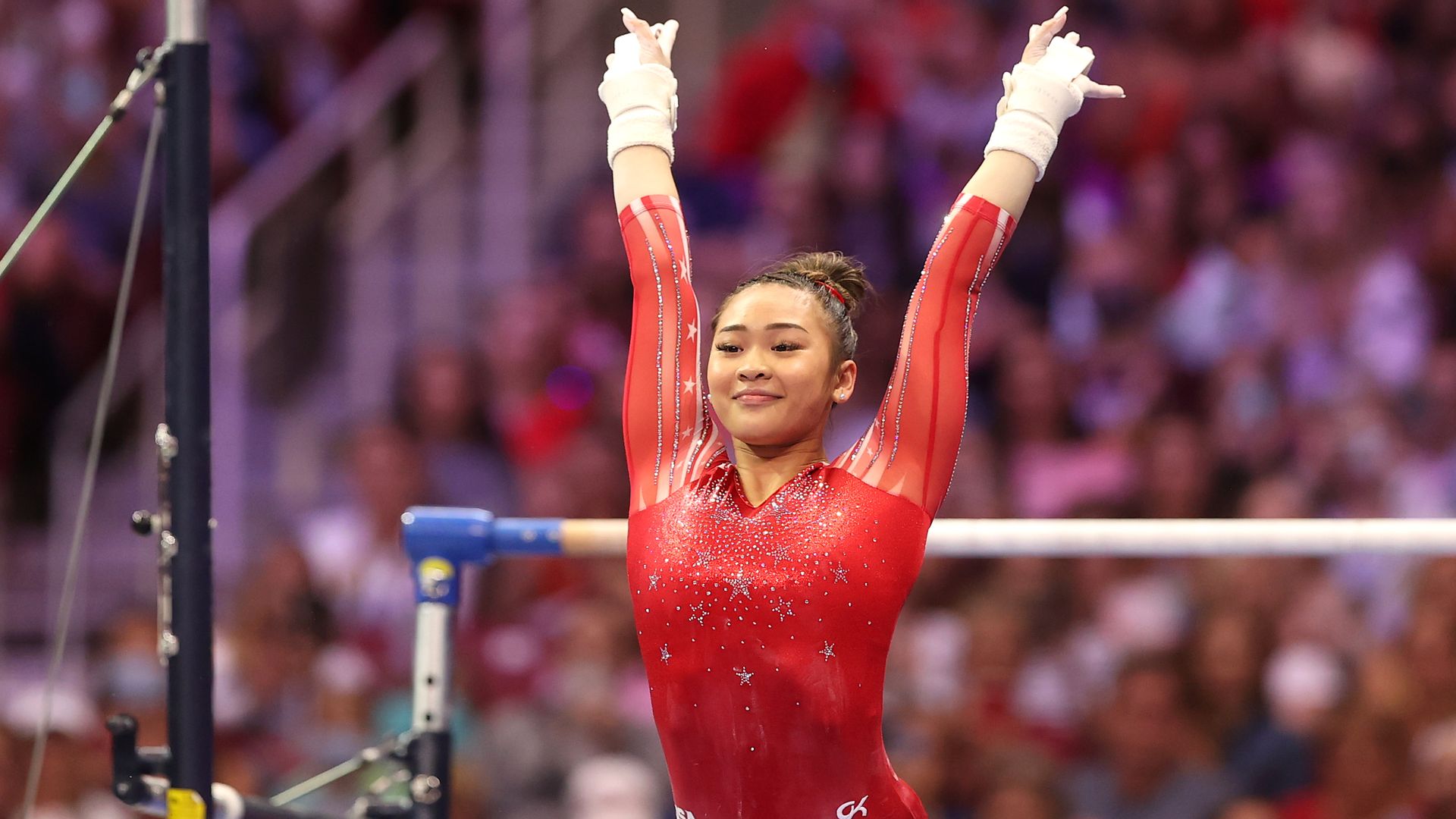 Suni Lee raises her hands in the air after finishing the uneven bars