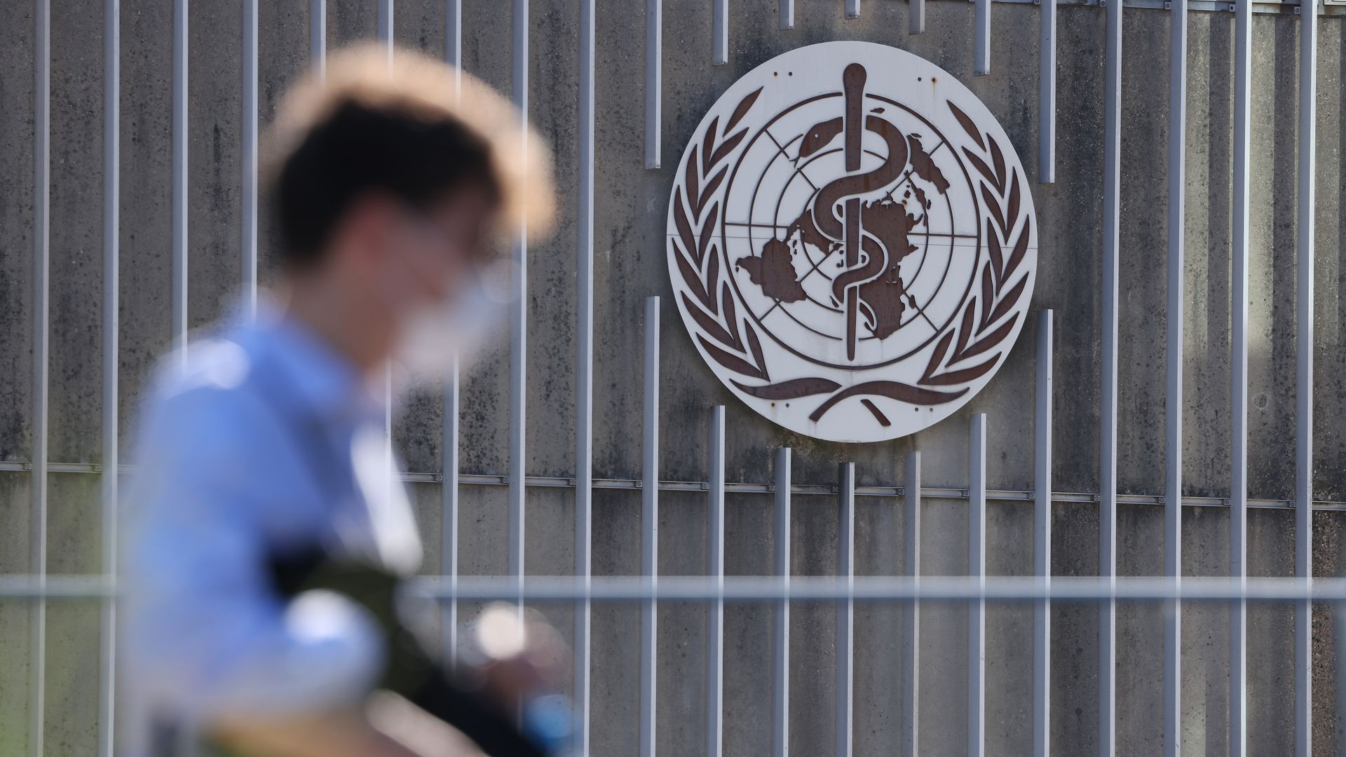 A man walks past the entrance of the World Health Organization, marked by its logo