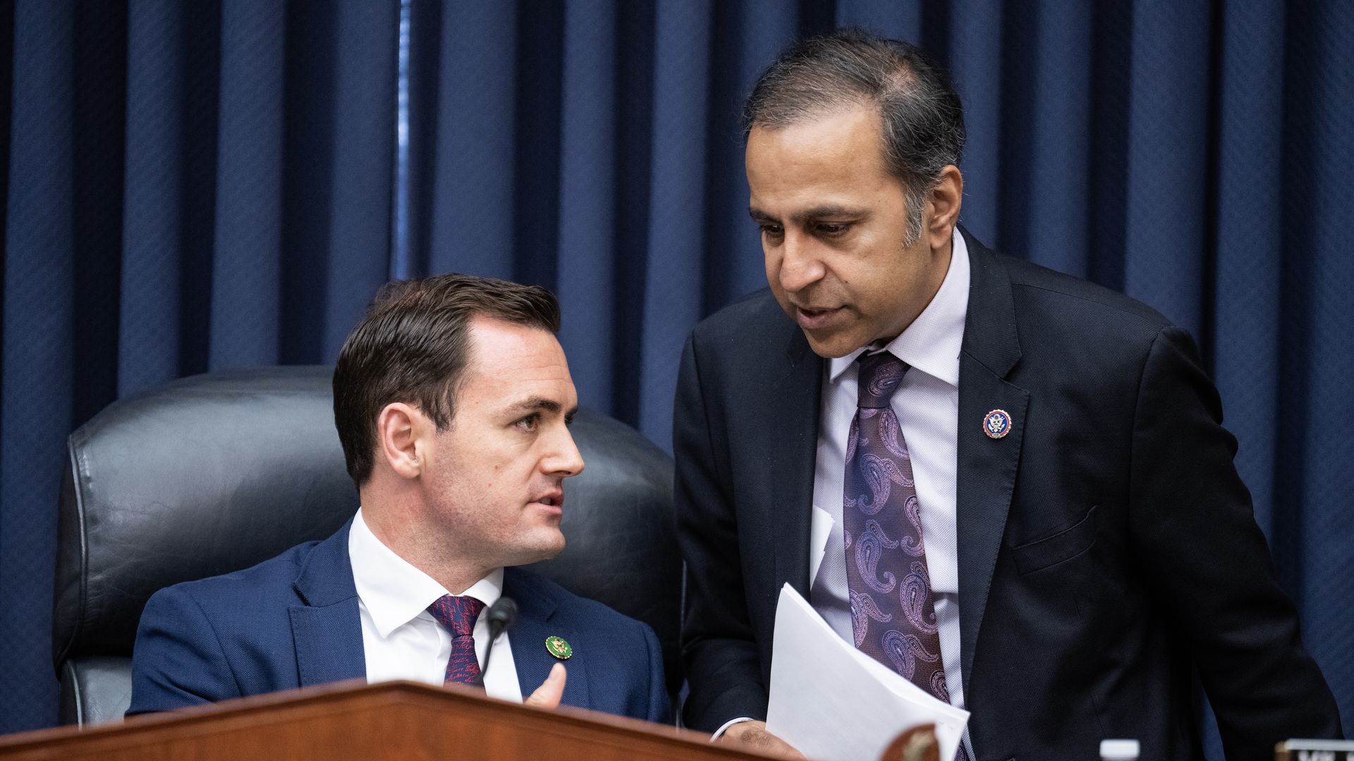 Two people wearing suits and ties talking