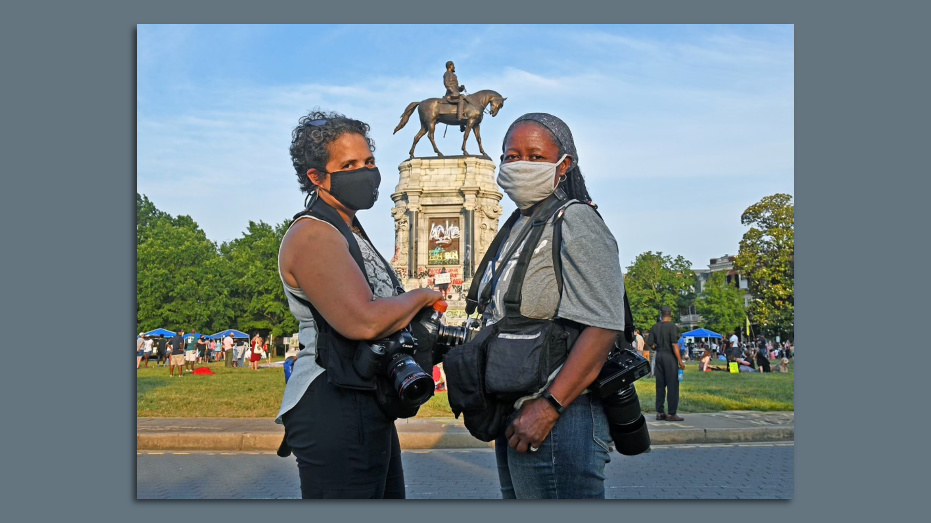 Two women stand in front of the graffiti covered Lee statue 