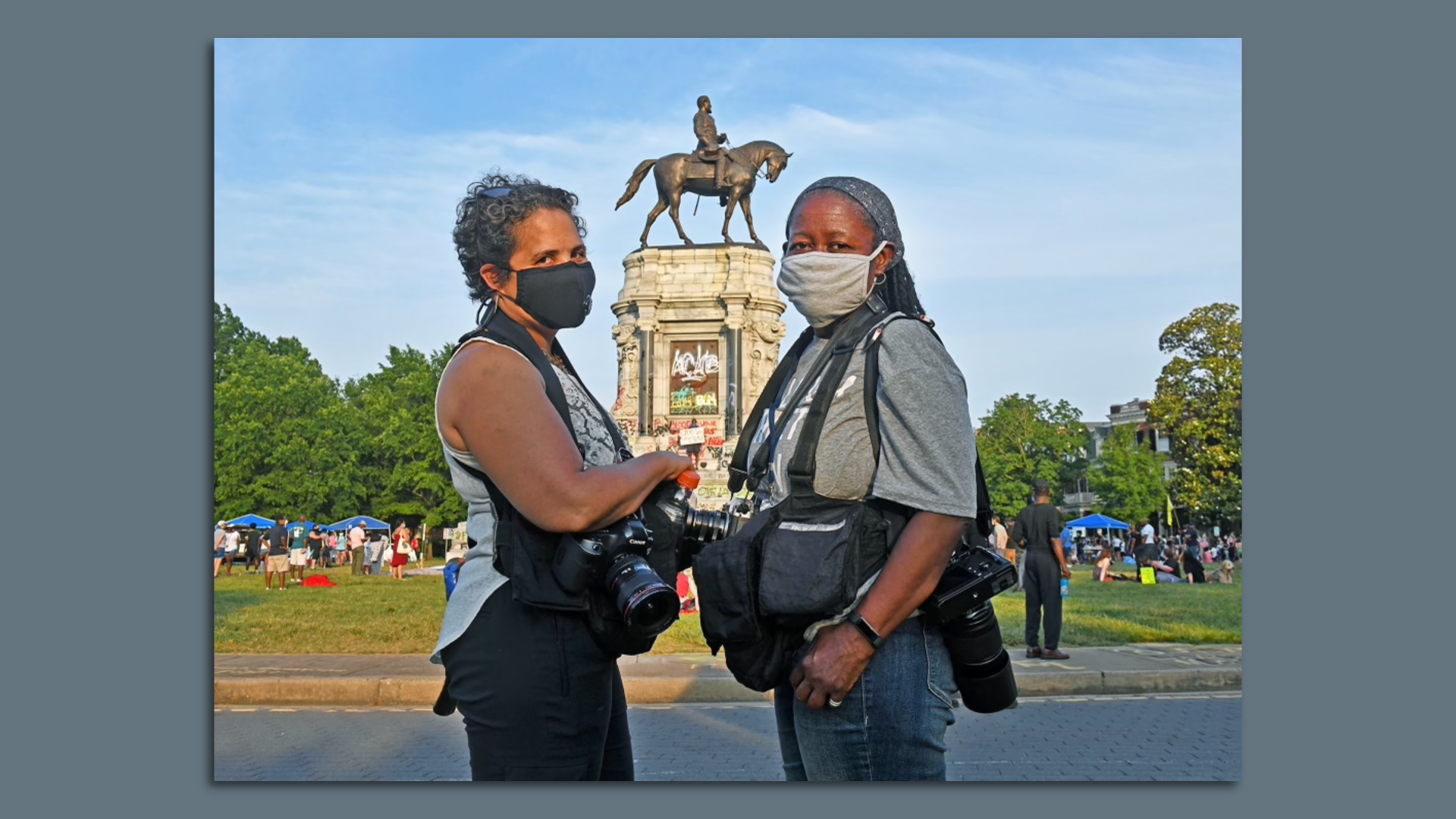Two women stand in front of the graffiti covered Lee statue