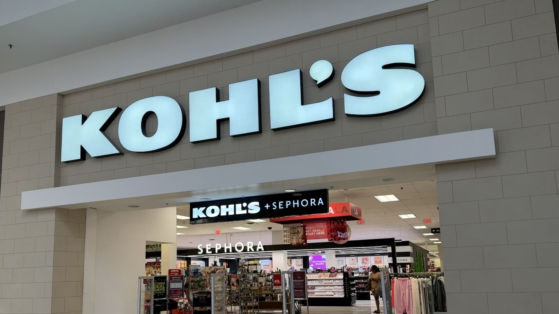 Exterior of a Kohl's department store in a mall, featuring a large turquoise Kohl's sign above the entrance. Inside, a Kohl's plus Sephora sign leads to a Sephora section with displays and shoppers.