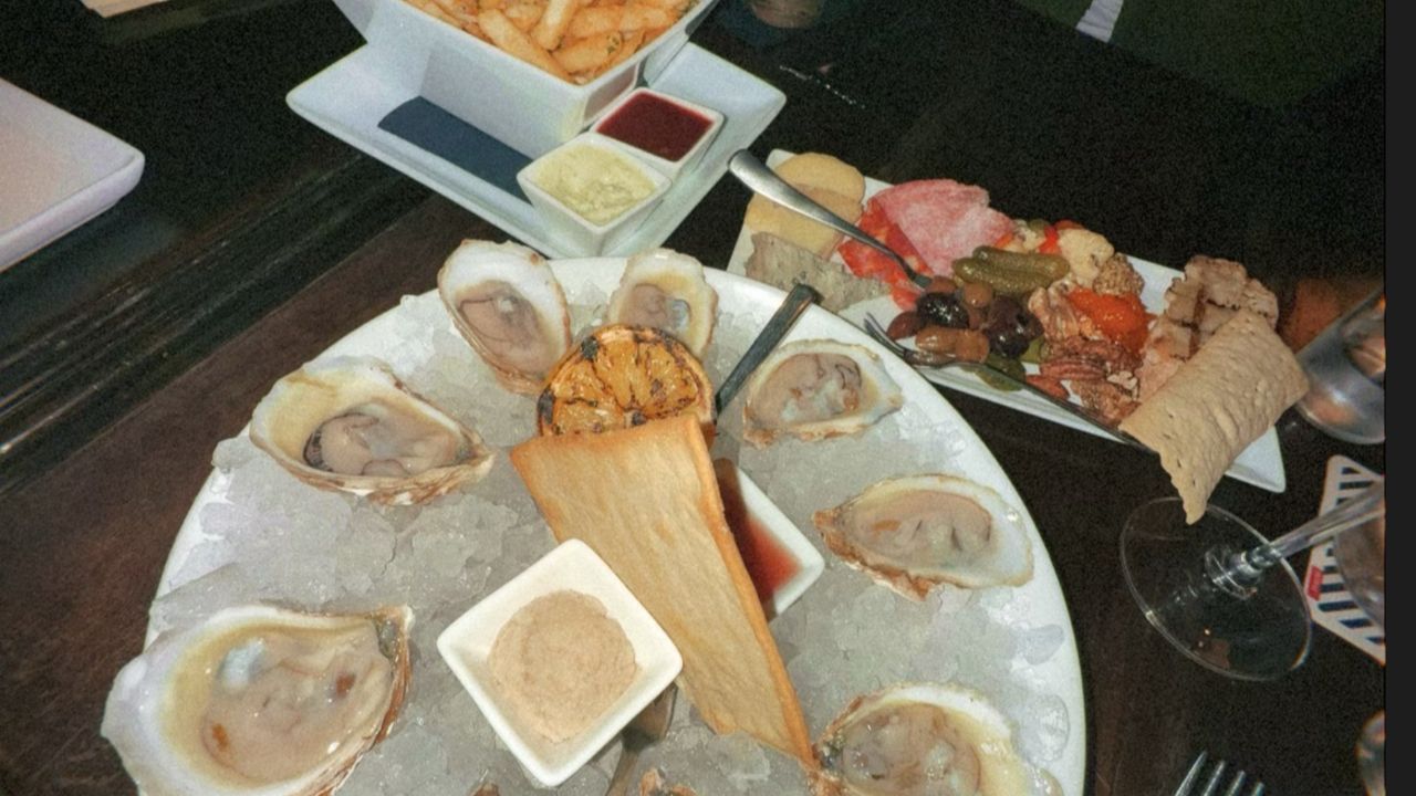 Plate of oysters on ice with lemon wedge and horseradish sauce, plate of mixed charcuterie, pickles, olives, and crackers, and a bowl of seasoned fries with two dipping sauces.
