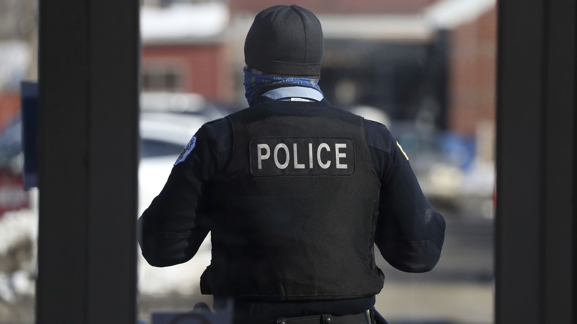 Photograph of a police officer from behind, with a cap on and a vest marked "police."