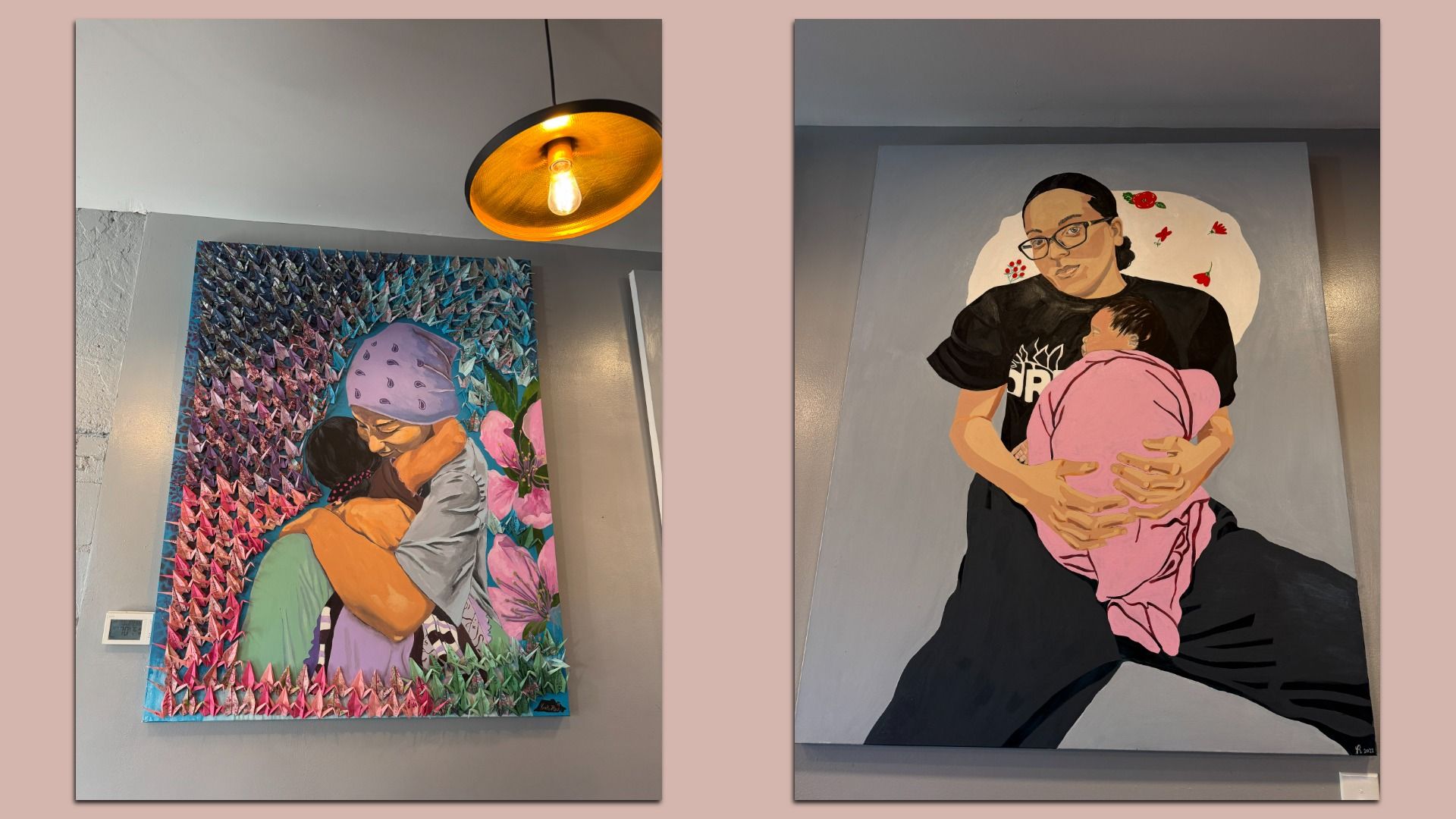 Two large paintings on a gray wall. Left: a mother wearing a purple headscarf embracing a child, amid a colorful background with folded paper cranes. Right: a woman with glasses holding a baby wrapped in pink, against a gray backdrop.