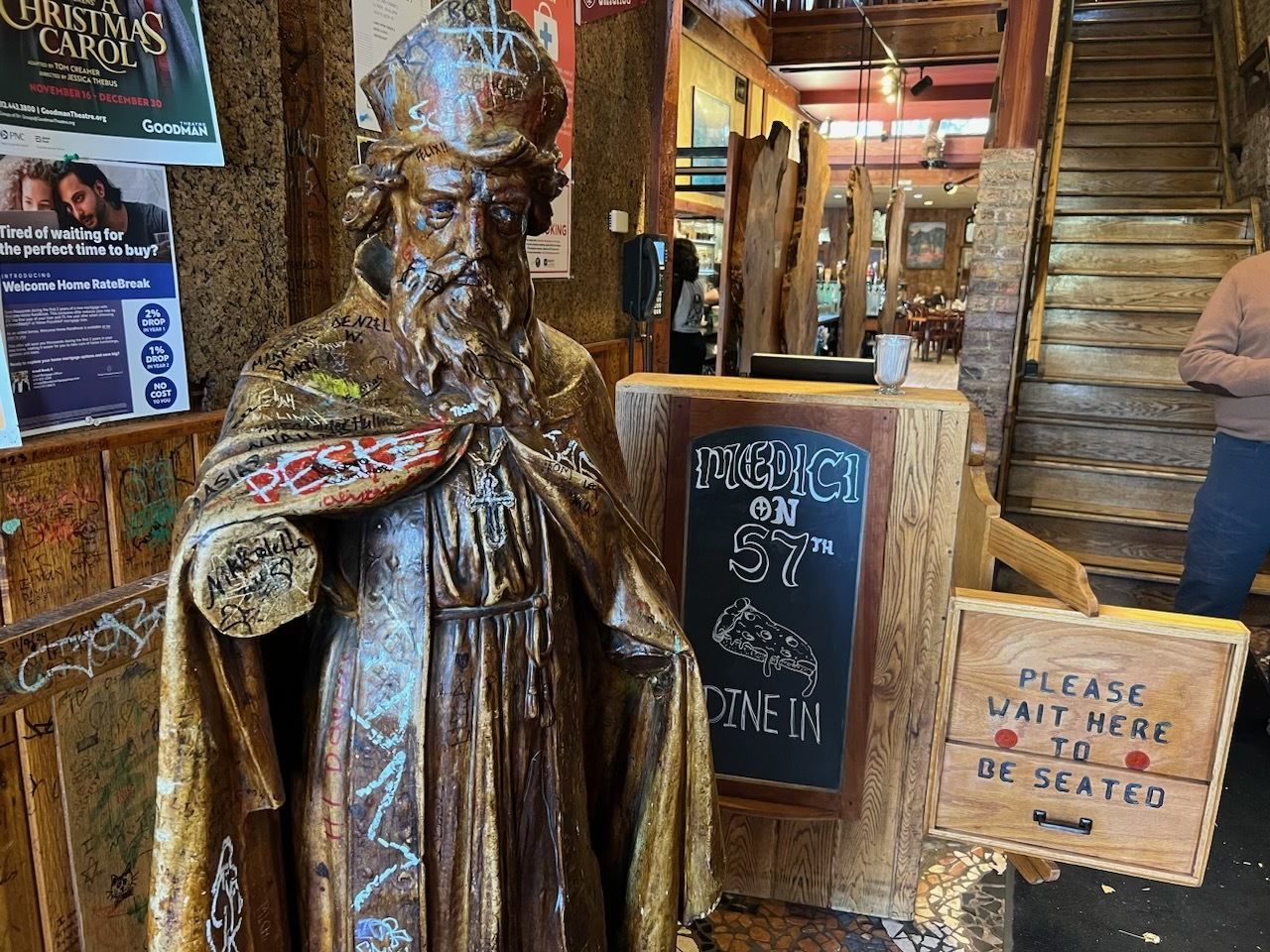 Photo of a statue of a king next to a chalkboard sign at front of a restaurant 