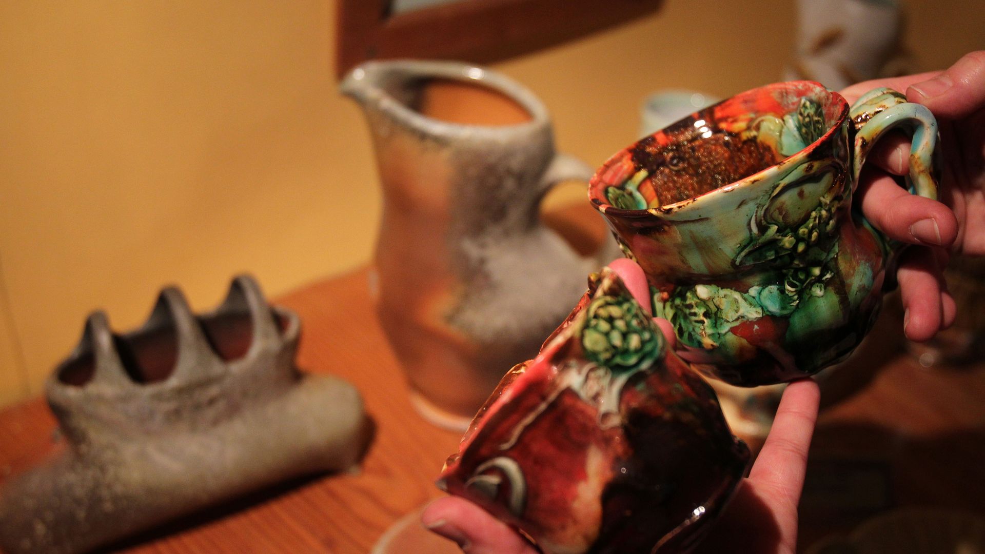 A picture of someone holding a ceramic mug with others in the background.