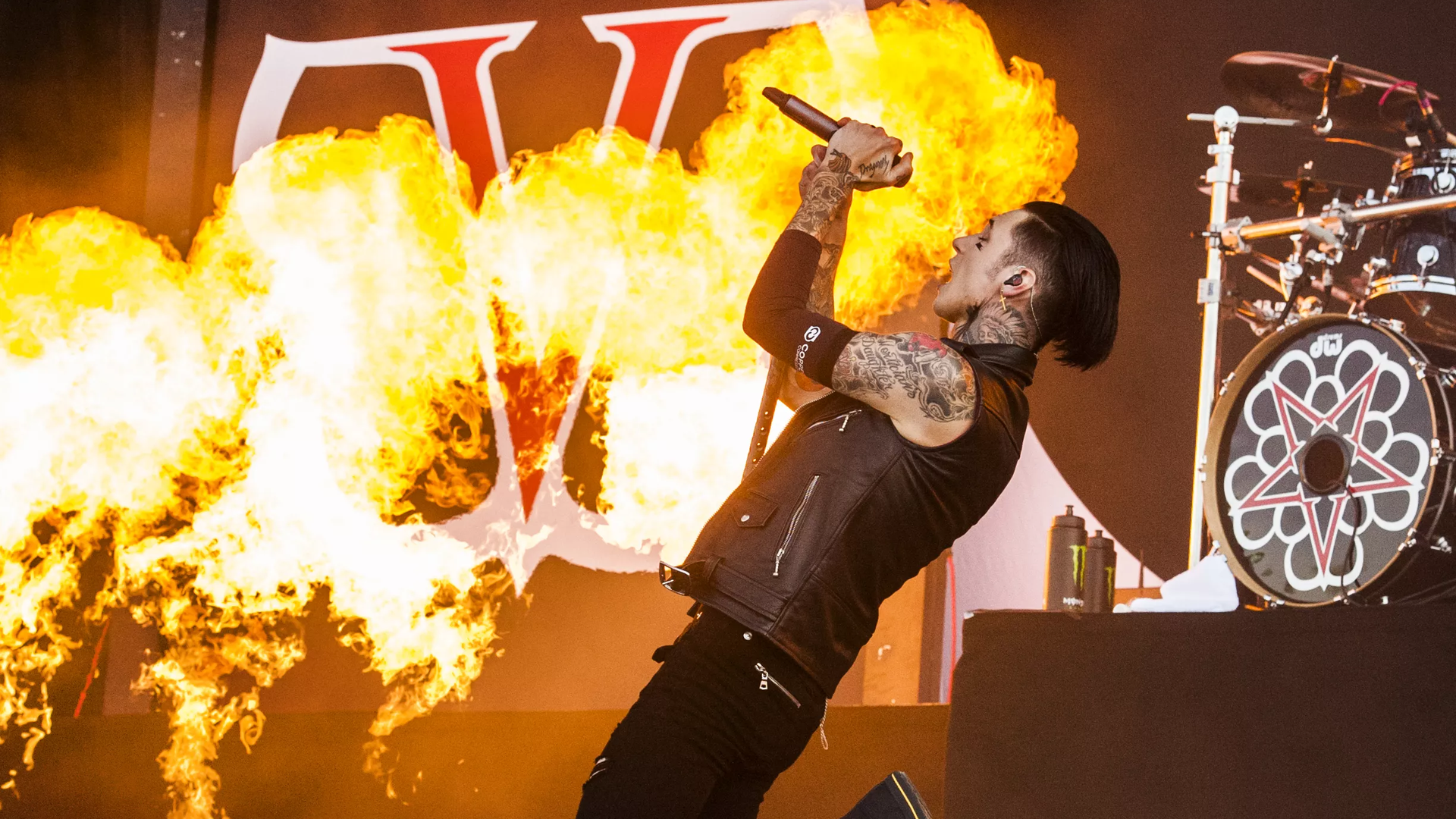 A performer sings into a mic with fire in the background