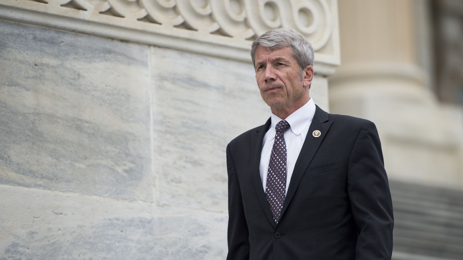 Man in dark suit walks down steps steps at U.S. Capitol building.